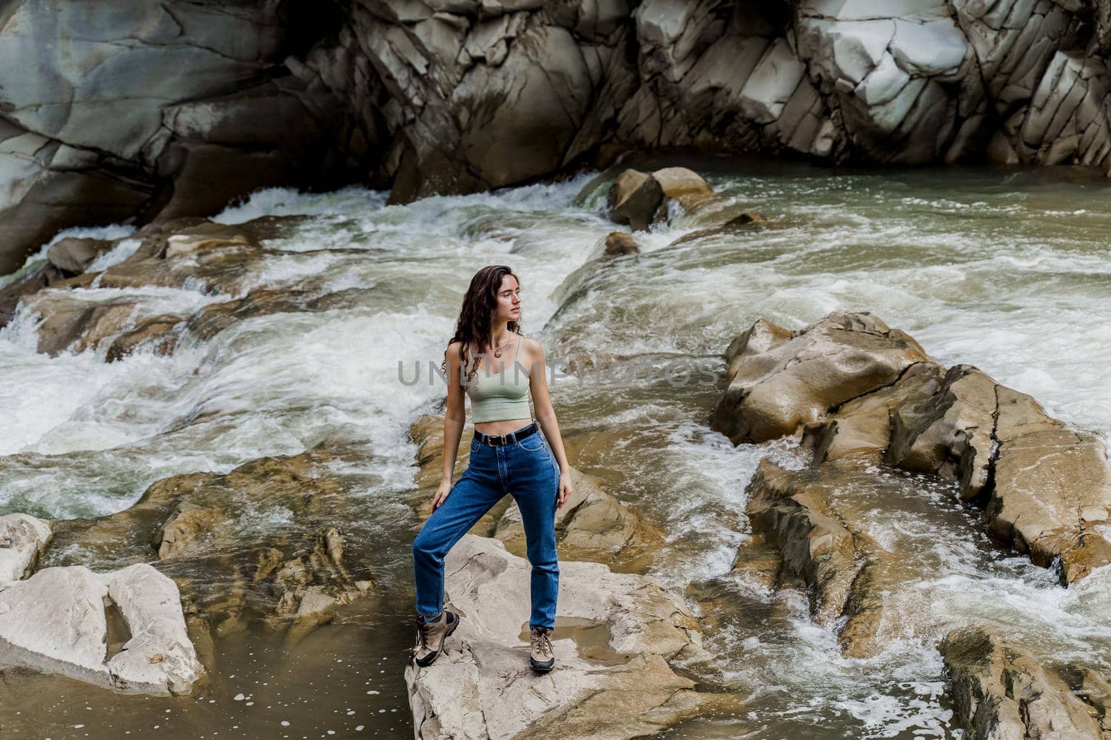 Girl is travelling in Karpathian mountains and feeling freedom. Waterfall in mountain river. Cascade waterfall and beautiful young woman