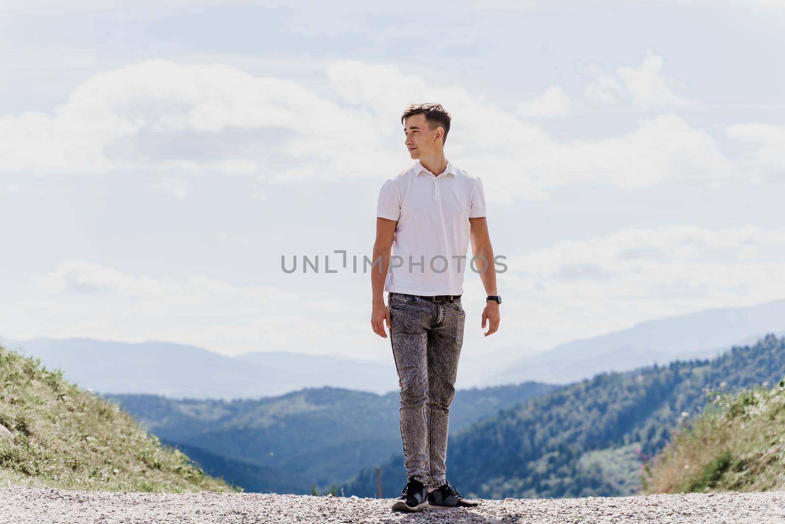 Handsome man is walking on the green hills background. Advert for travel agency. Tourism. Travelling in the mountains.