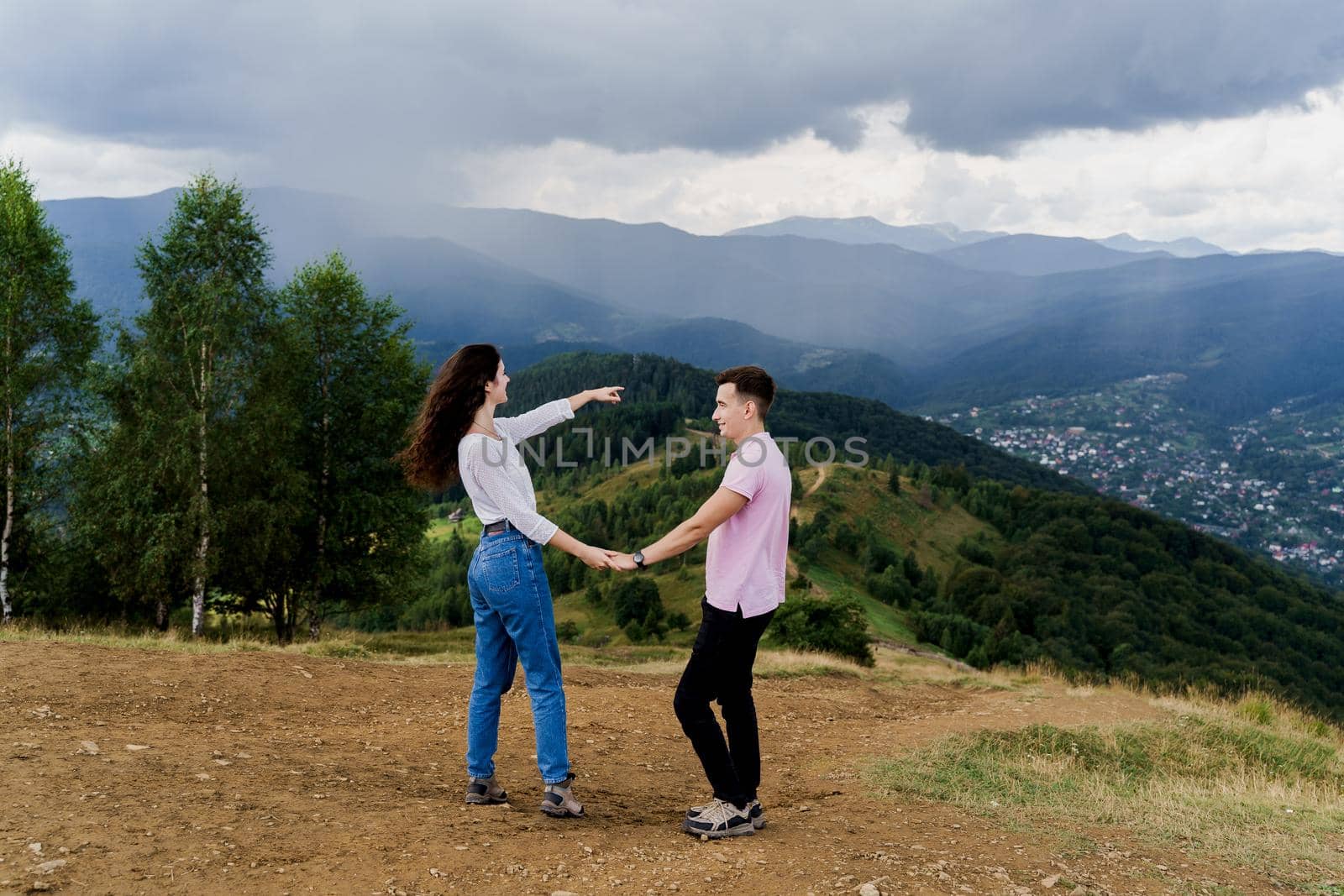 Girl points her boyfriend at rain far away. Couple looking at the mountain hills before raining. Feeling freedom together in Karpathian mountains.