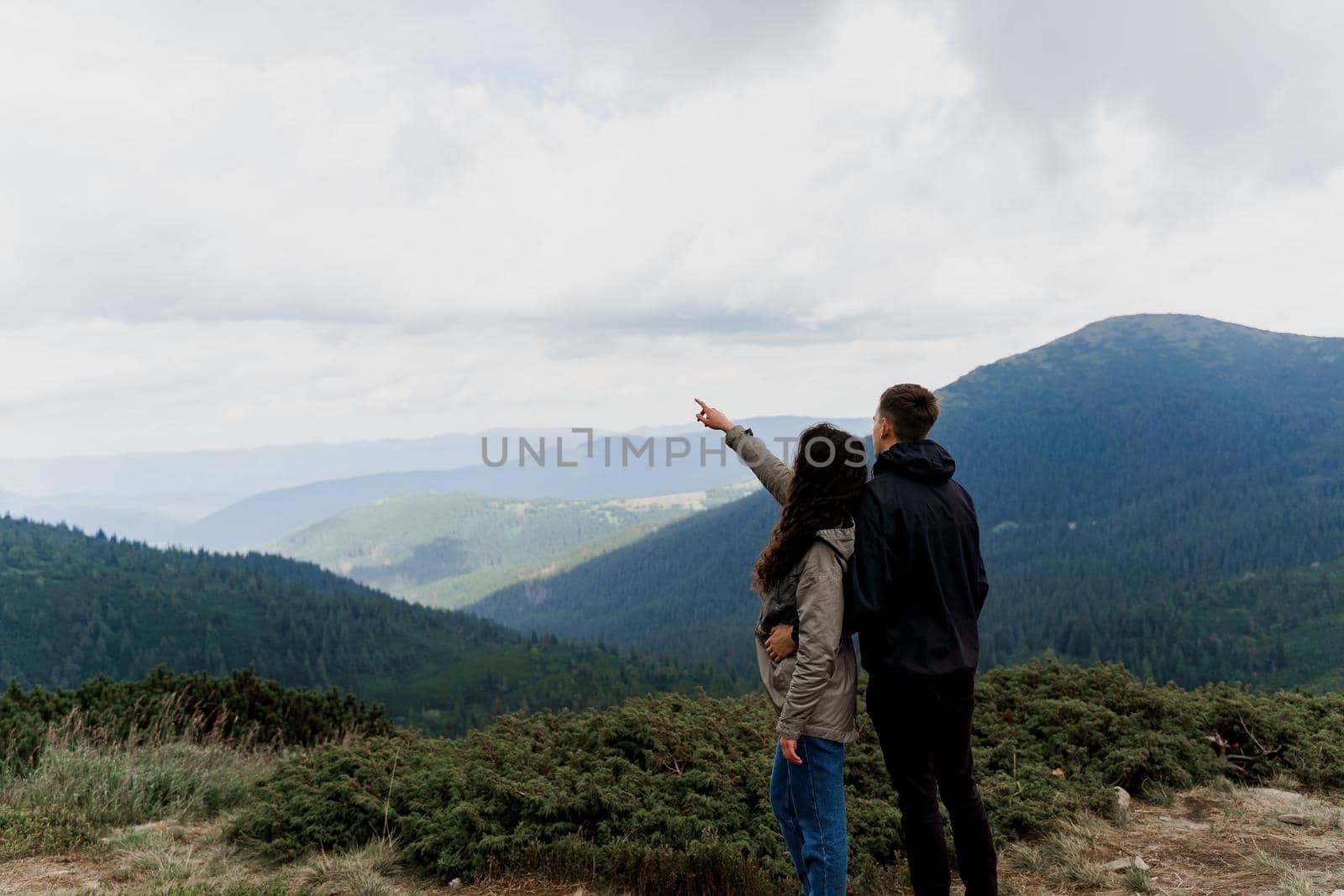 Couple at the peak of the mountain. Girl is pointing to the sky. Lifestyle of travelling people. Love story in the mountains