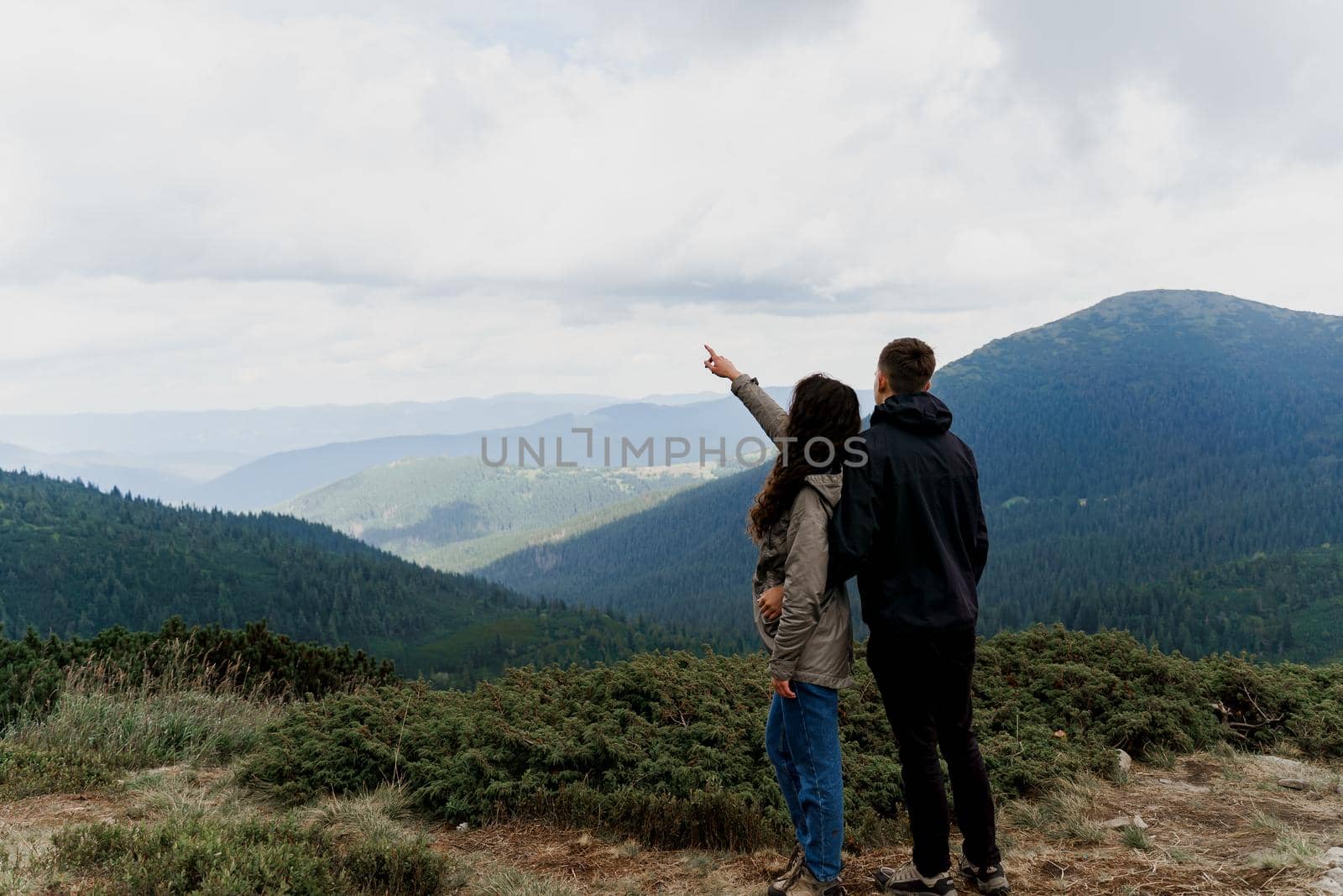 Couple at the peak of the mountain. Girl is pointing to the sky. Lifestyle of travelling people. Love story in the mountains. by Rabizo