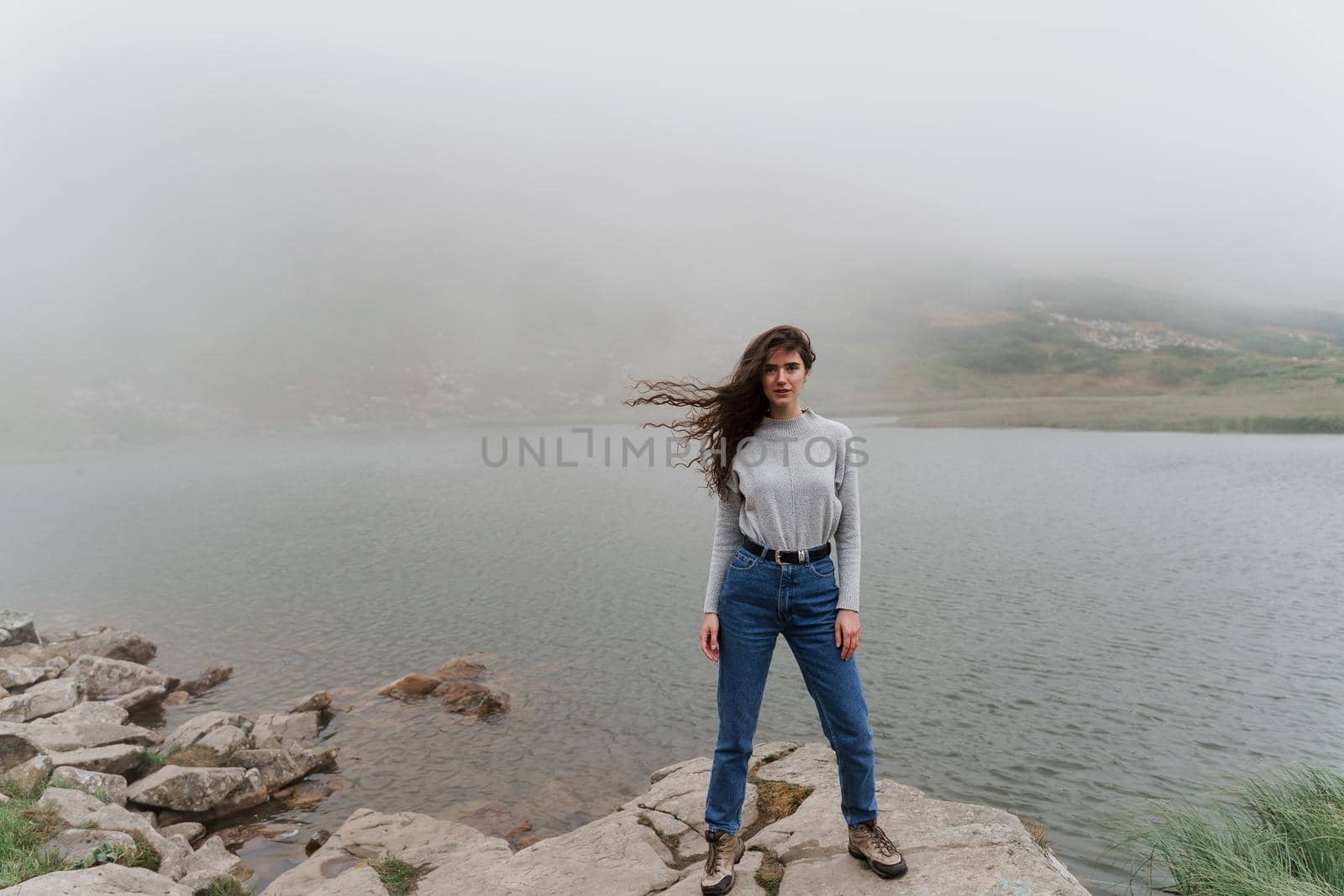 Lake at the peak of the mountain. Foggy lake. Girl is posing on the rocks.