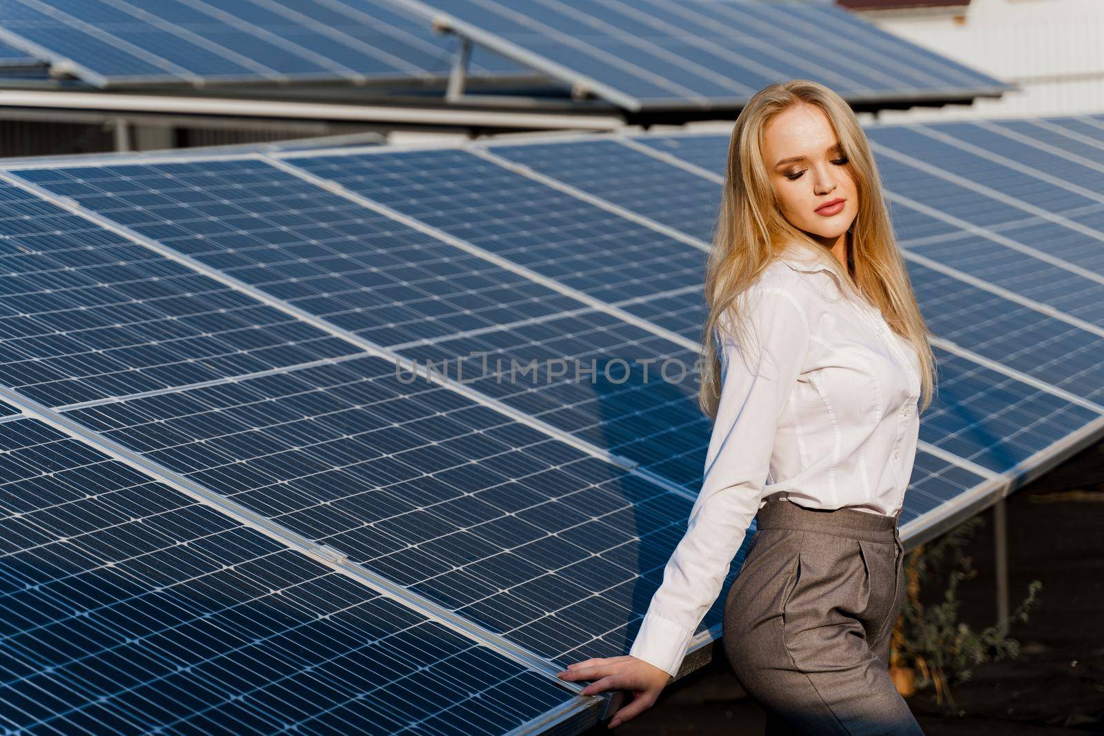 Woman leans on solar panels. Blonde dressed white formal shirt on the power plant. Free electricity for home. Green energy