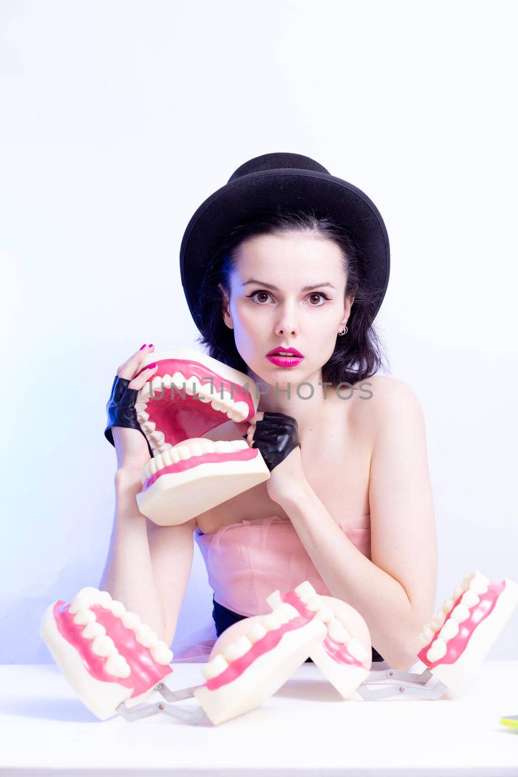 A woman in a dress and hat sits at a table and holds a mock-up of her teeth. High quality photo