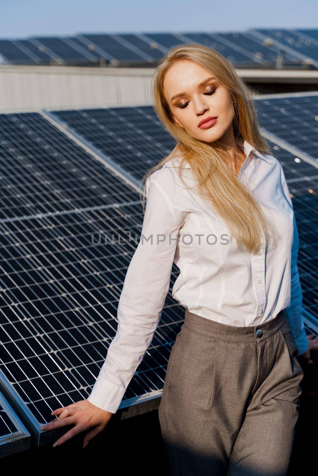 Close-up portrait of blonde model near solar panels. Free electricity for home. Green energy. Solar cells power plant business