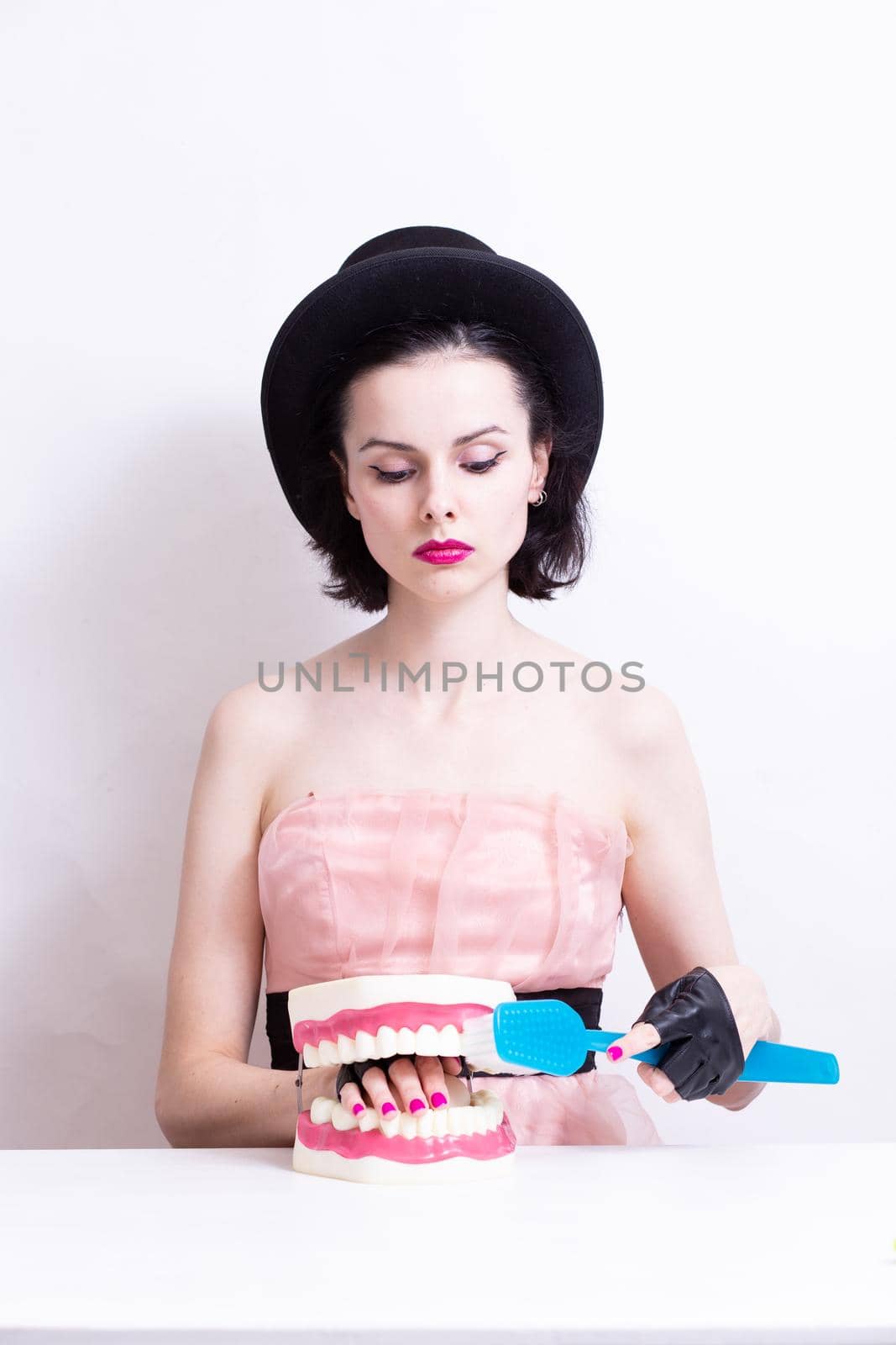 A woman in a dress and hat sits at a table and holds a mock-up of her teeth. High quality photo