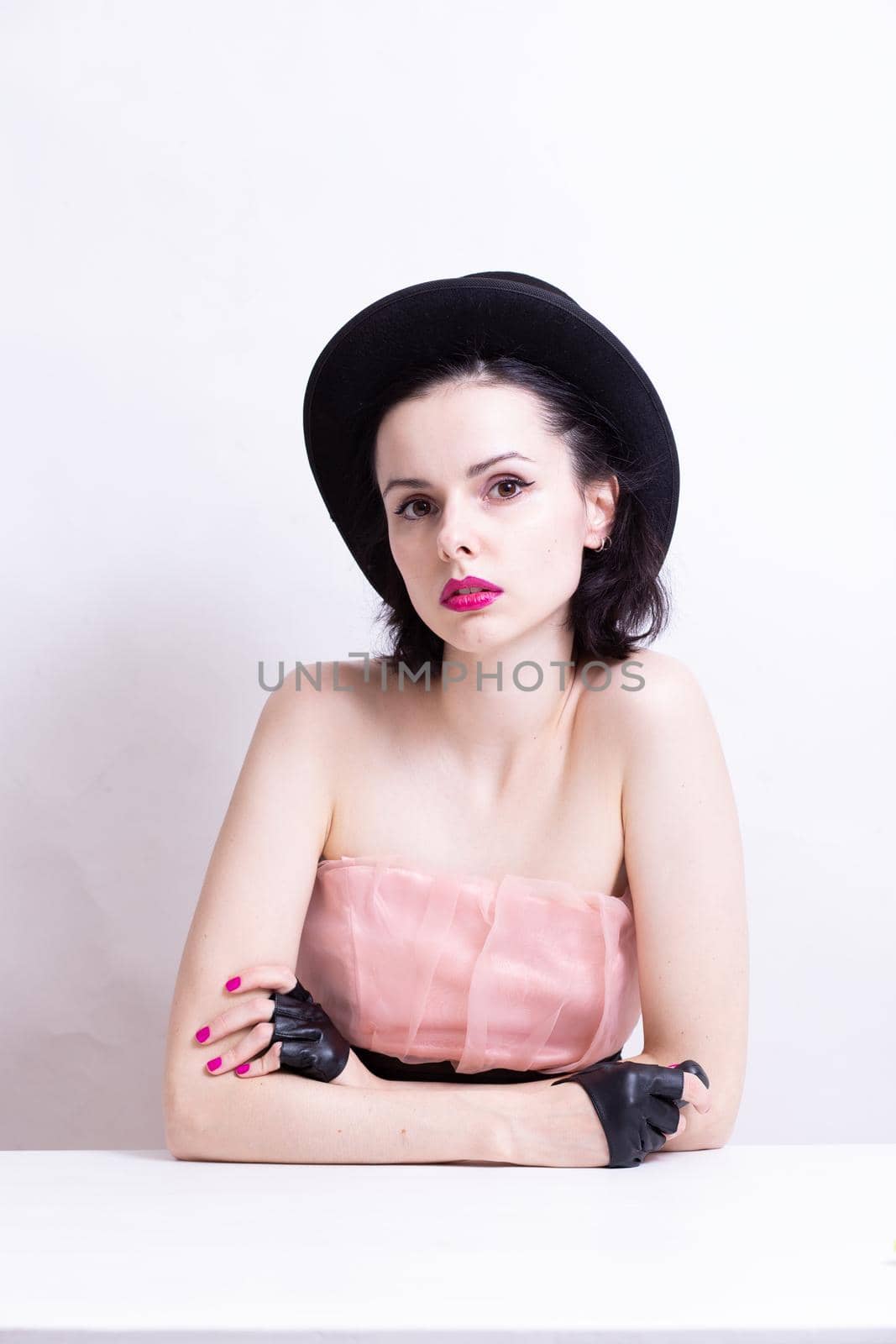 beautiful woman with pink lips in a dress, hat and gloves sits at the table. High quality photo