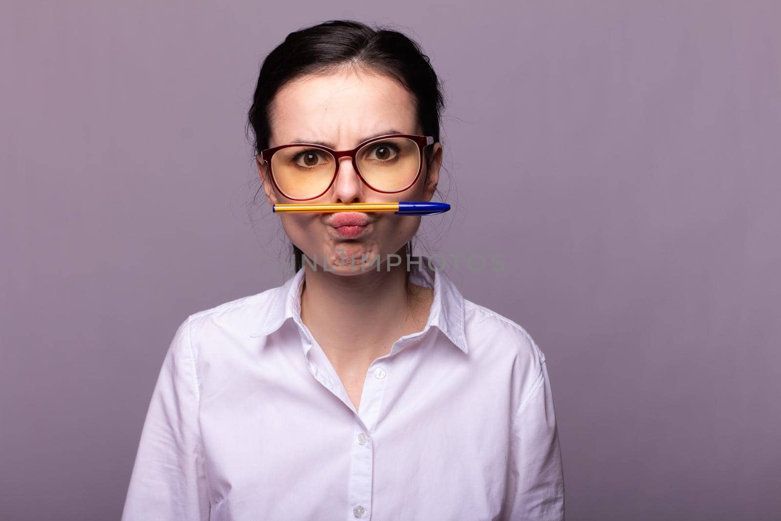 woman in a white shirt and glasses holds a pen with her mouth by shilovskaya