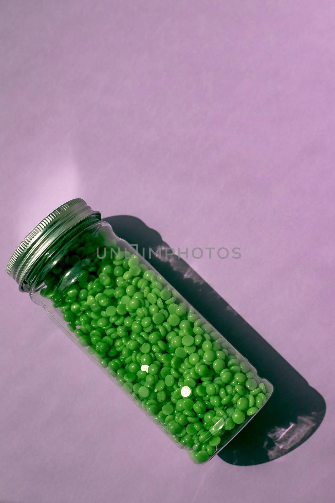 green wax for depilation in granules. on a purple background. jar with wax on isolated background.