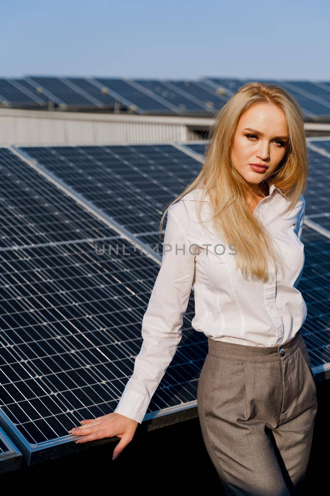 Woman leans on solar panels. Blonde dressed white formal shirt on the power plant. Free electricity for home. Green energy.