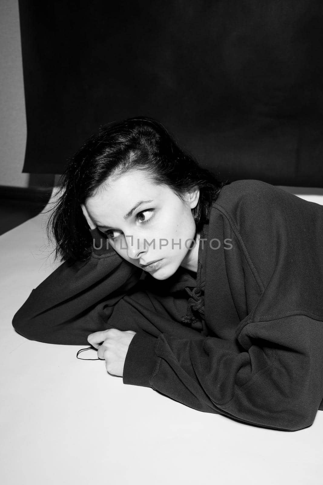 a woman in a black hoodie lies on the floor, black and white photography by shilovskaya