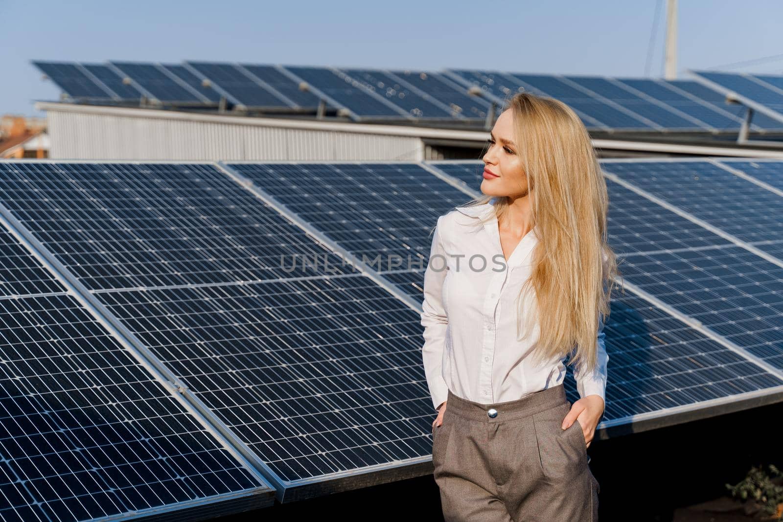 Woman leans on solar panels. Blonde dressed white formal shirt on the power plant. Free electricity for home. Green energy