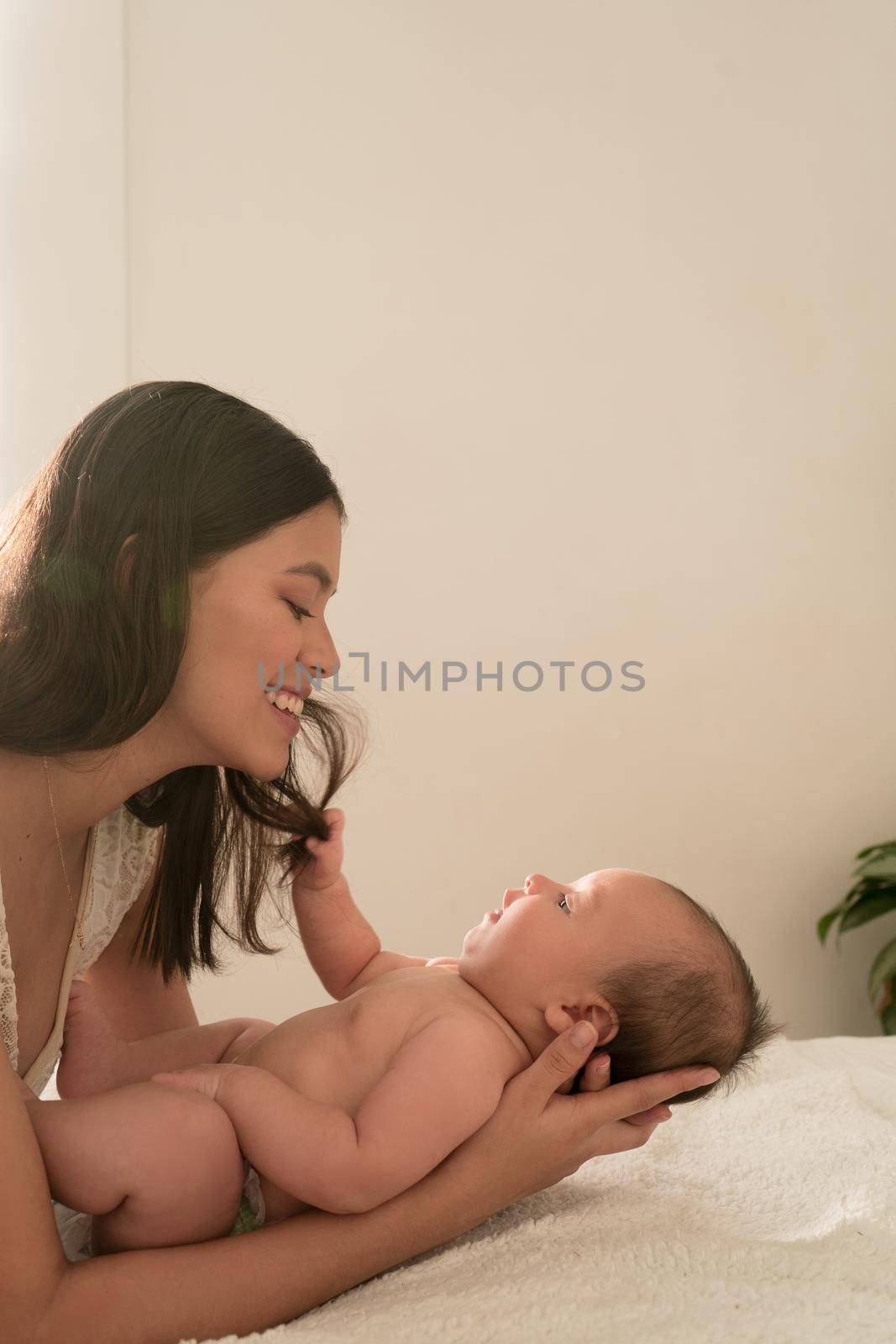 Latin young mother love play happy with baby on the bed at home. High quality photo vertical photo style life