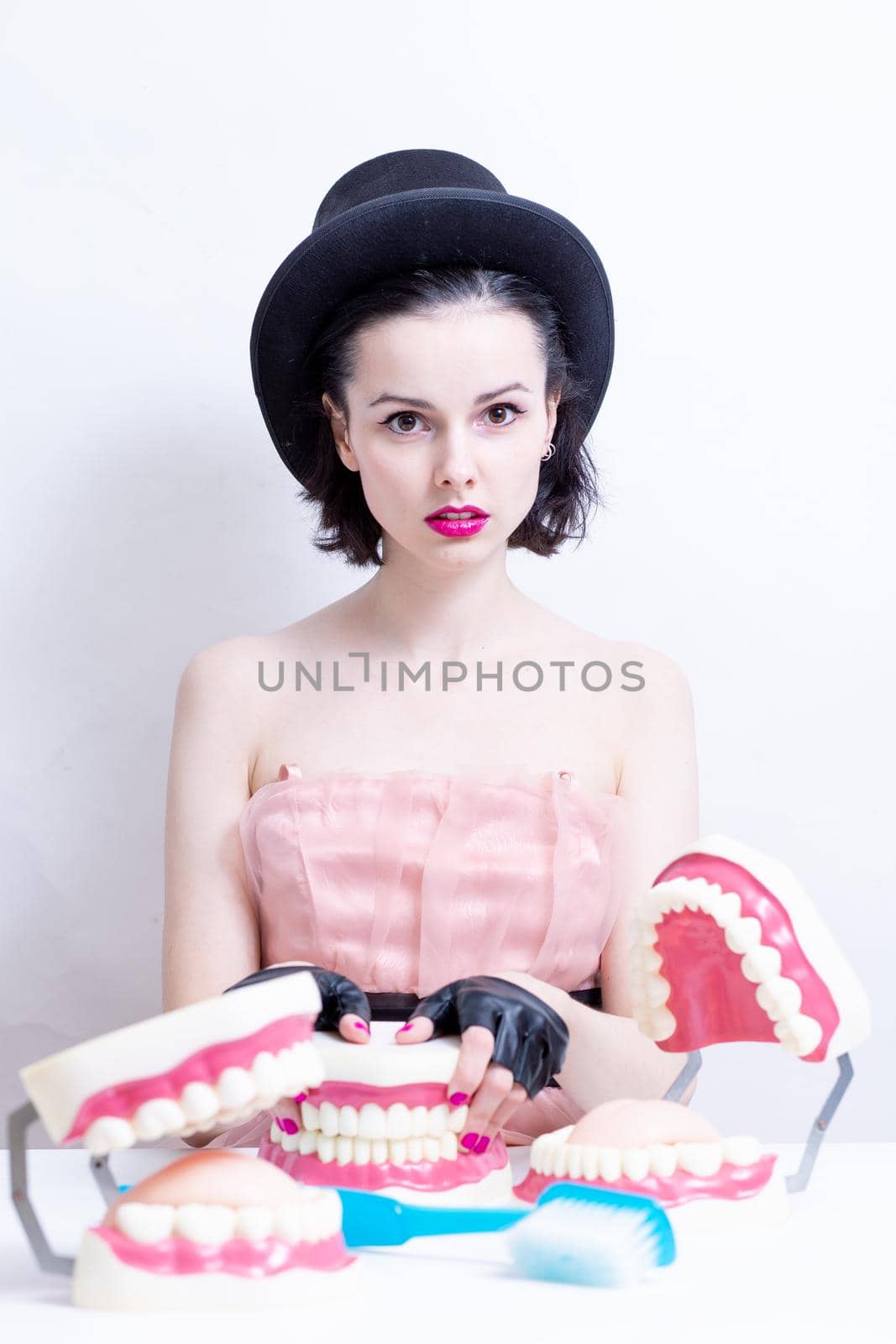 A woman in a dress and hat sits at a table and holds a mock-up of her teeth. High quality photo