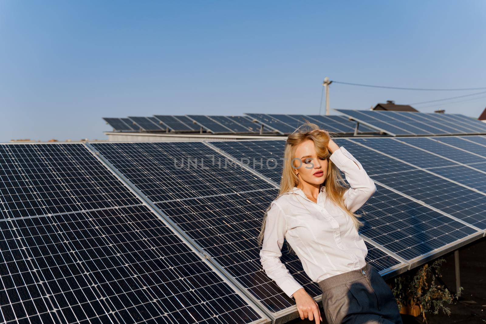 Woman leans on solar panels. Blonde dressed white formal shirt on the power plant. Free electricity for home. Green energy.