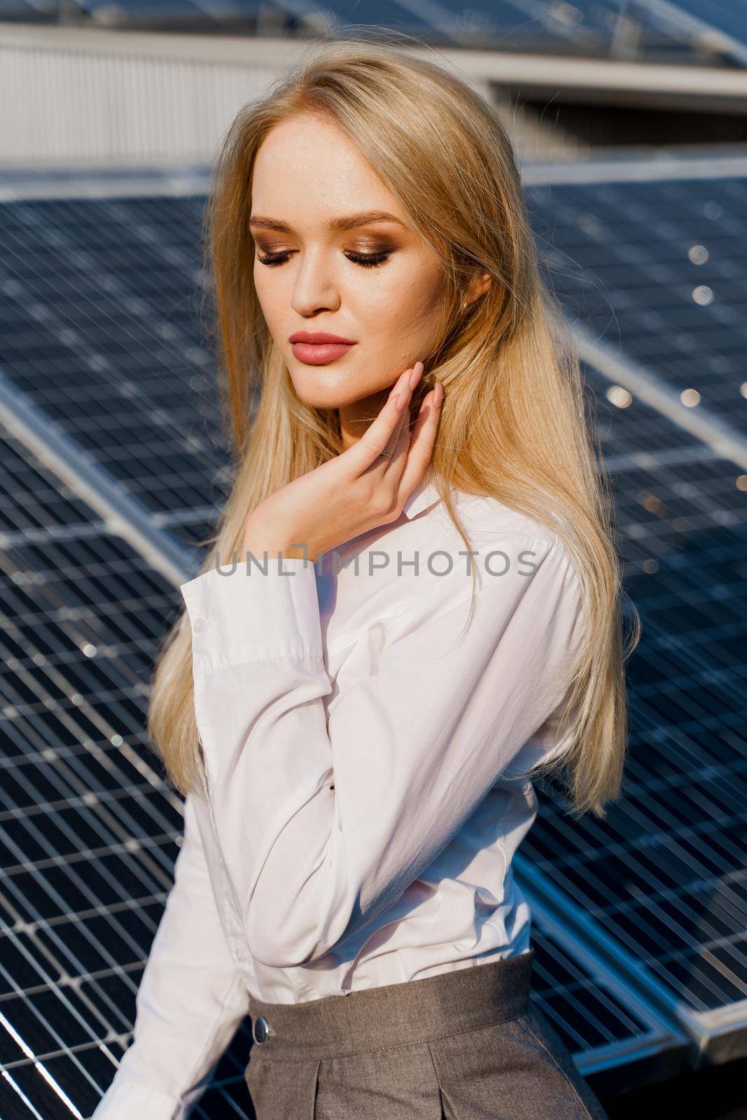 Close-up portrait of blonde model near solar panels. Free electricity for home. Green energy. Solar cells power plant business
