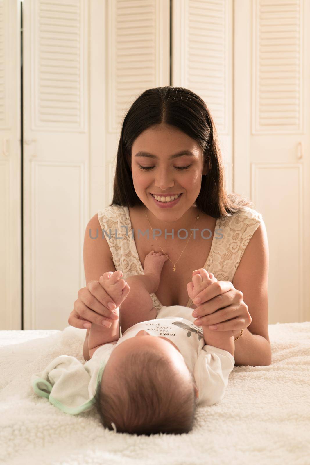 Latin young mother play happy with baby on the bed at home by FranciscoStockLife