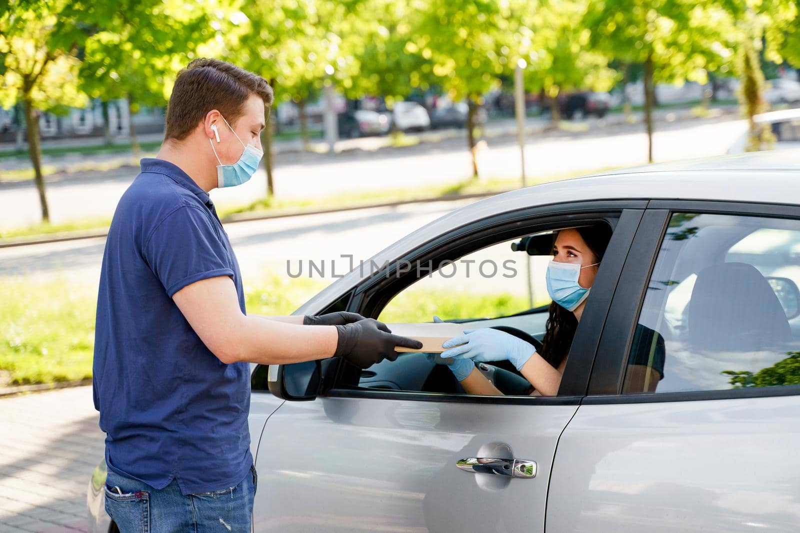 Food delivery courier gives pizza to woman in eco car. Tasty pizza with salami, cheese, tomatoes in cardoard box. Giving food trought car window