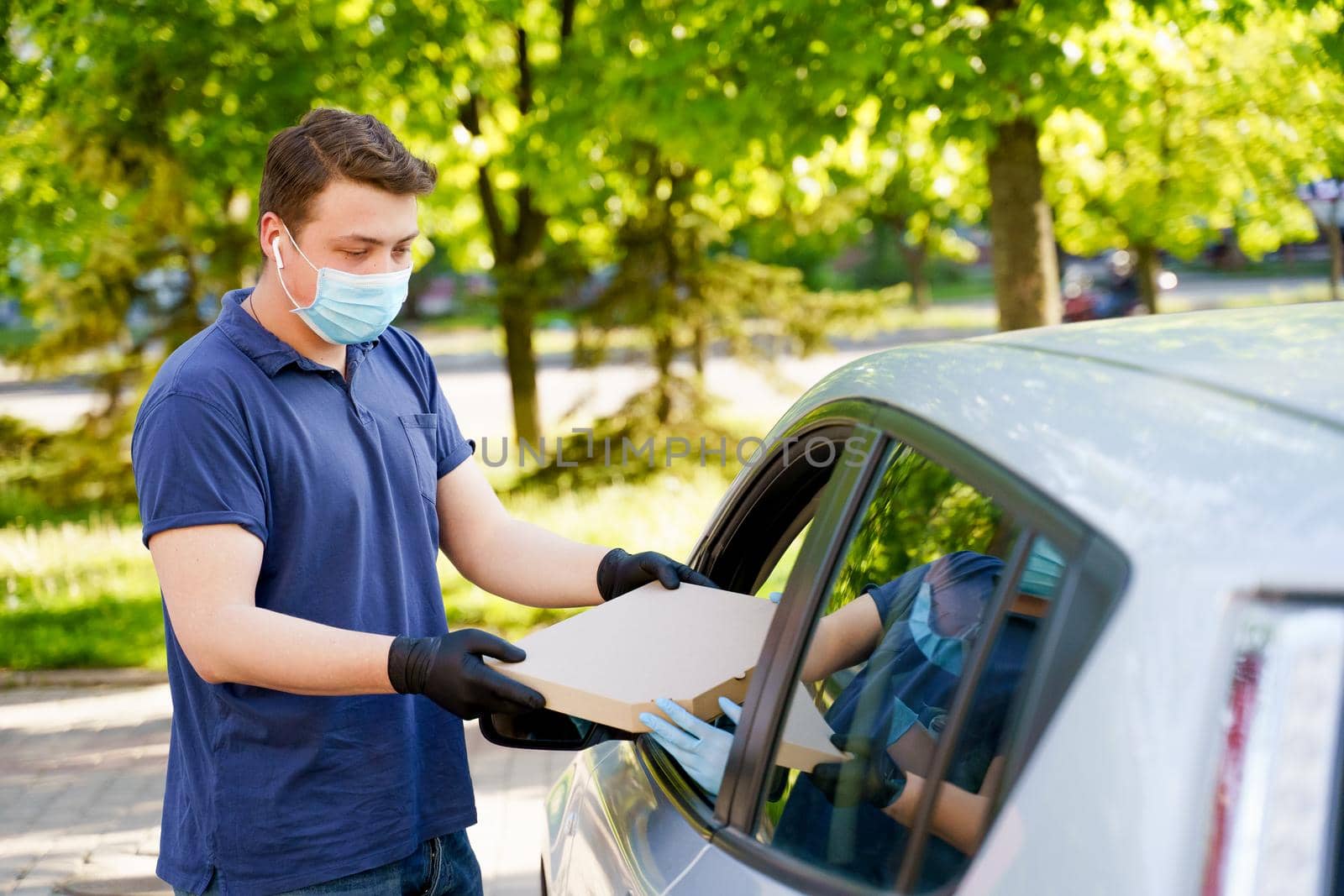 Safety pizza delivery from pizzeria trought car window during quarantine covid 19. Business woman in medical mask and gloves gets food in carton box