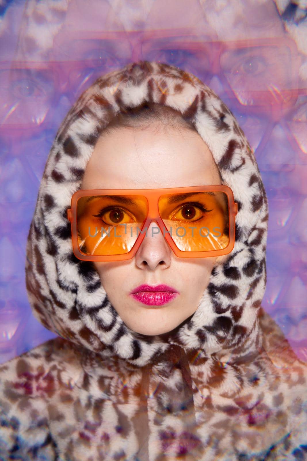 Art portrait, a woman with pink lips in orange glasses and a leopard hoodie on a blue background. High quality photo