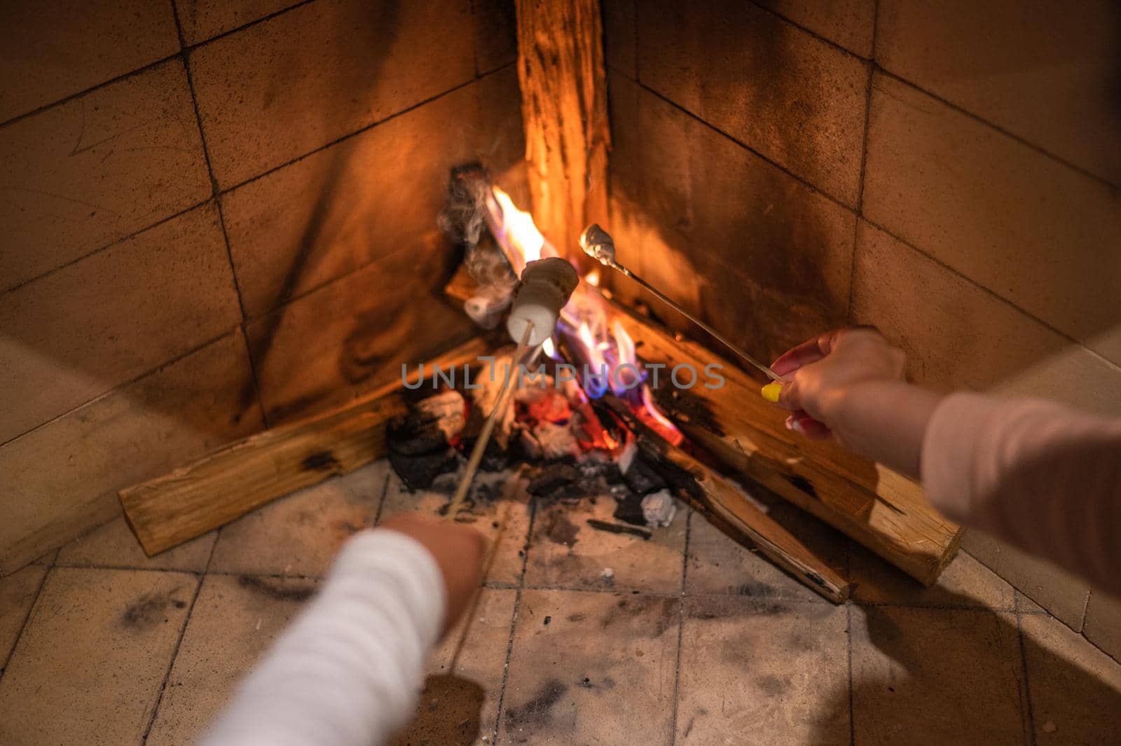 Marshmallows On Stick Roasting Over Campfire On Black Background. People take marshmallows around fireplace, enjoying their holiday. Hands of friends roasting marshmallows over fire in grill closeup