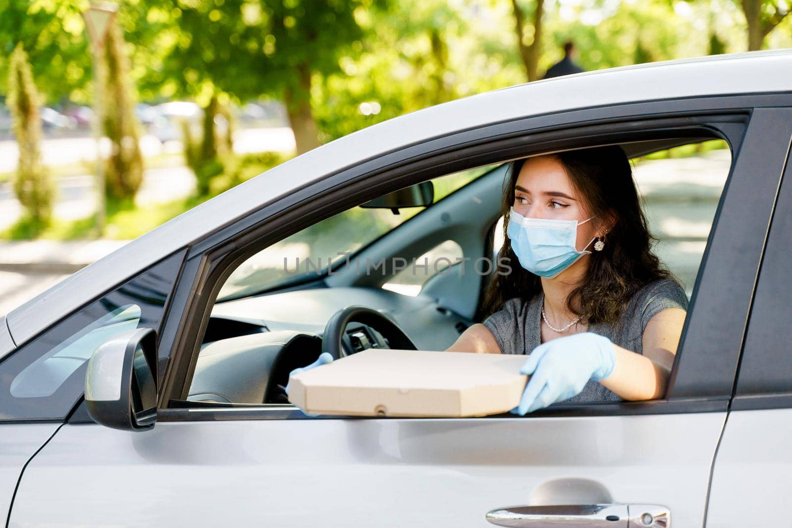 Student with pizza box in car with medical mask and gloves. Delivery food service drive by car. Safe food delivered according social distance