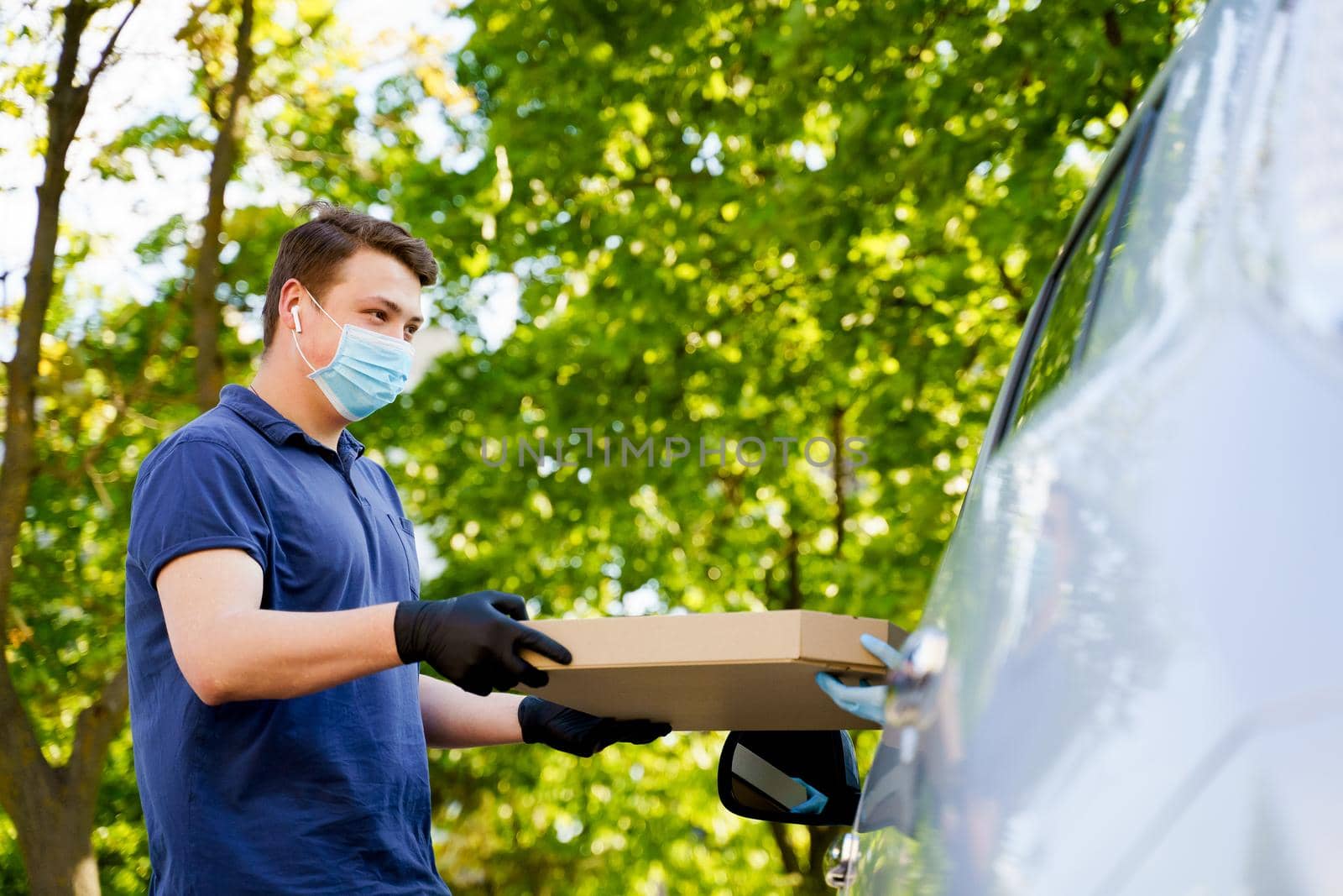 Young caucasian student works as food courier at quarantine covid 19 in delivery company. Convenient and safety delivering into car.