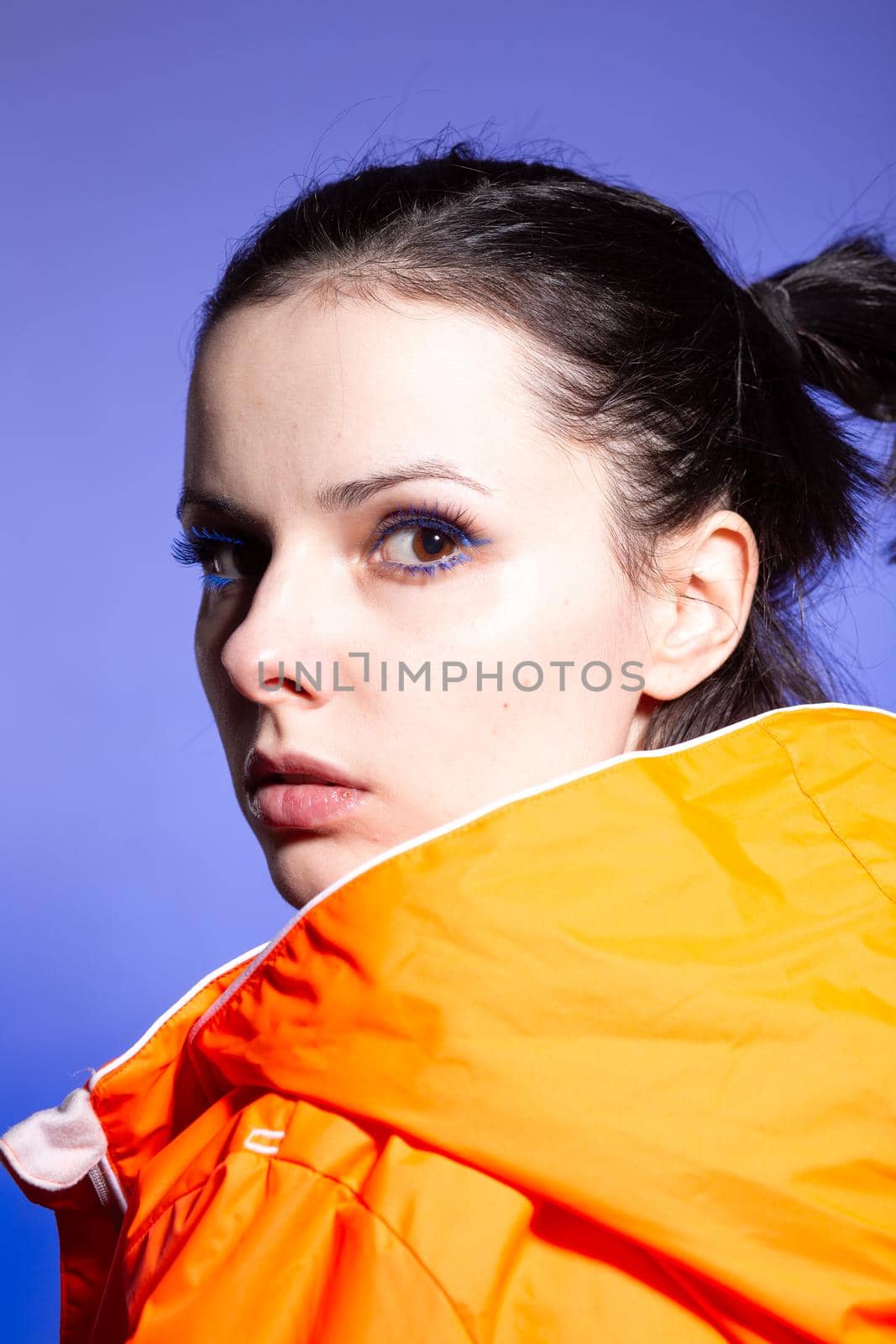 brunette woman in orange jacket, blue background. High quality photo