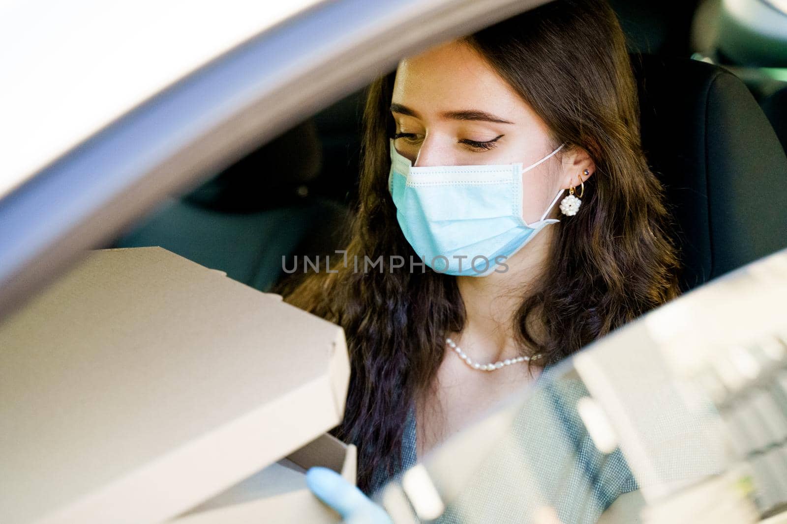 Lovely caucasian girl with green eyes looks at pizza and wants to eat. Courier in medical mask and gloves.
