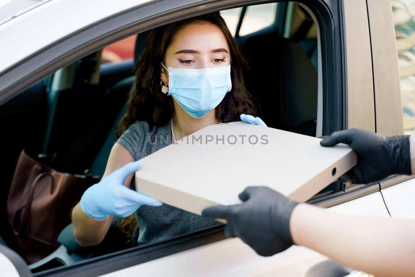 Food delivery courier gives pizza to woman in eco car. Tasty pizza with salami, cheese, tomatoes in cardoard box. Giving food trought car window. by Rabizo