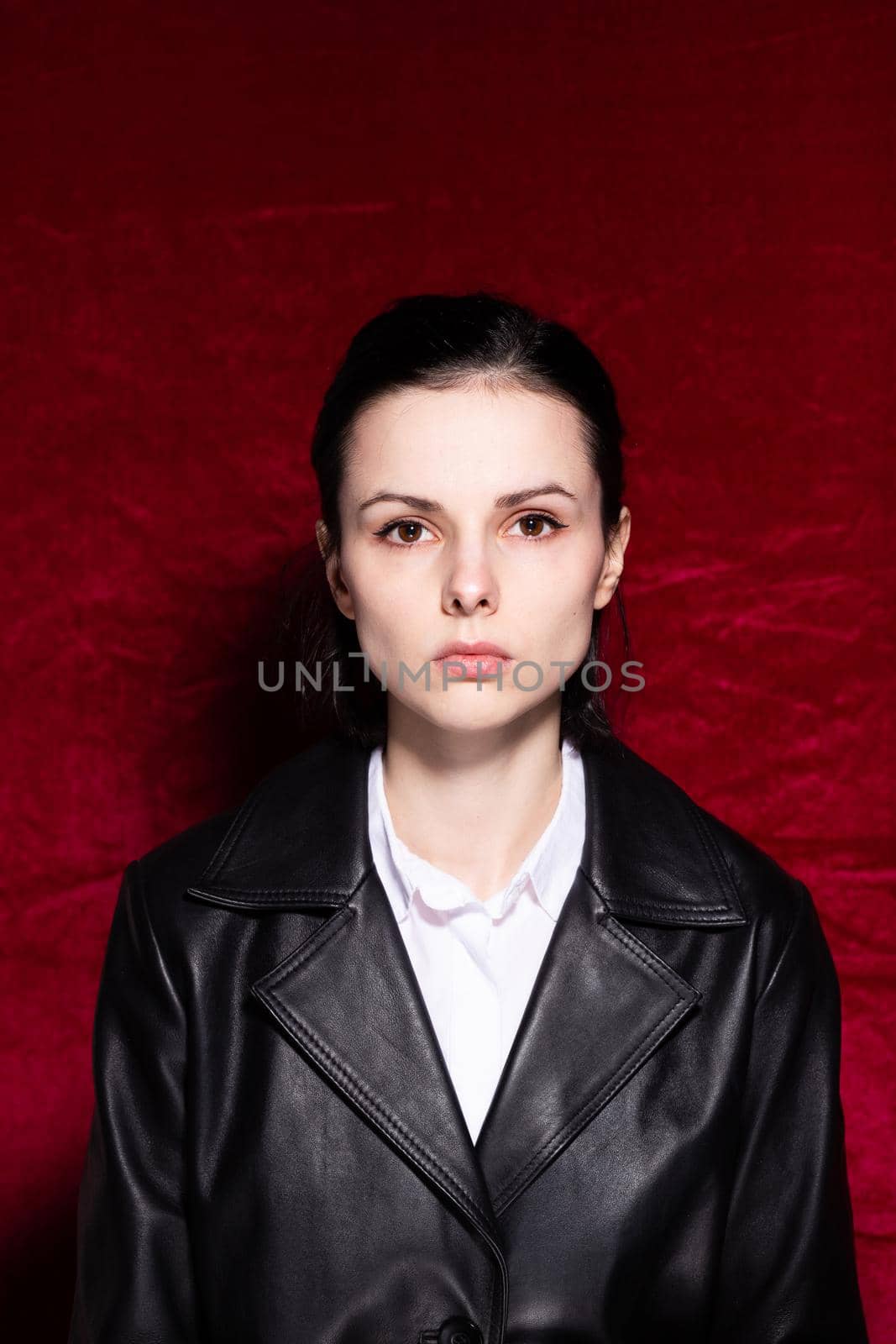 Woman in white shirt and black leather jacket on red velvet background. High quality photo