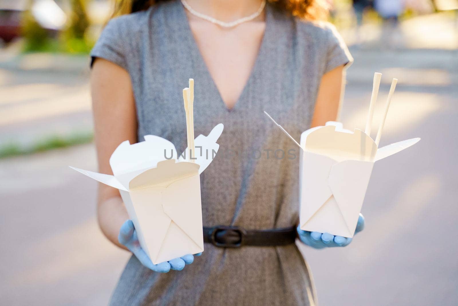 Closeup tasty food wok in box delivery. Girl holds udon noodles with tempuru, shrimps, soy sauce in hands. Chinese spicy food in disposable eco boxes by Rabizo