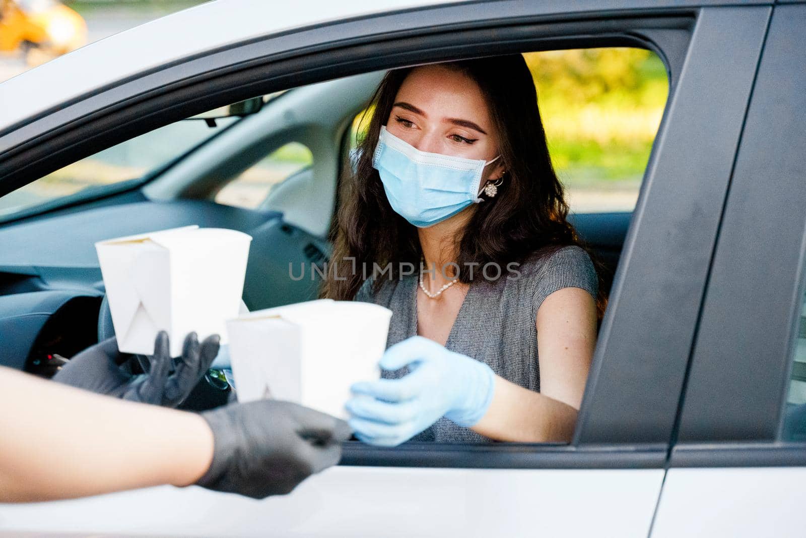 Young attractive girl in car in medical gloves and mask holds wok in box udon noodles in hands and smiles. Udon noodles in white box delivery