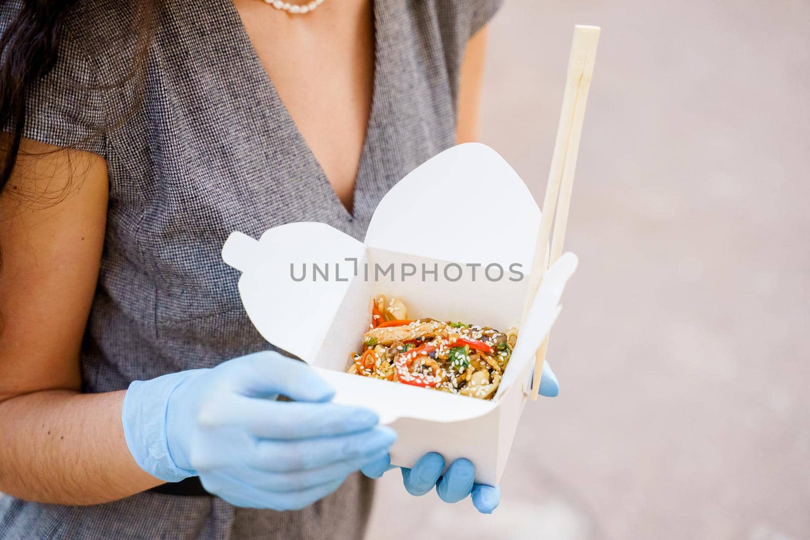 Closeup tasty food wok in box delivery. Girl holds udon noodles with tempuru, shrimps, soy sauce in hands. Chinese spicy food in disposable eco boxes. by Rabizo