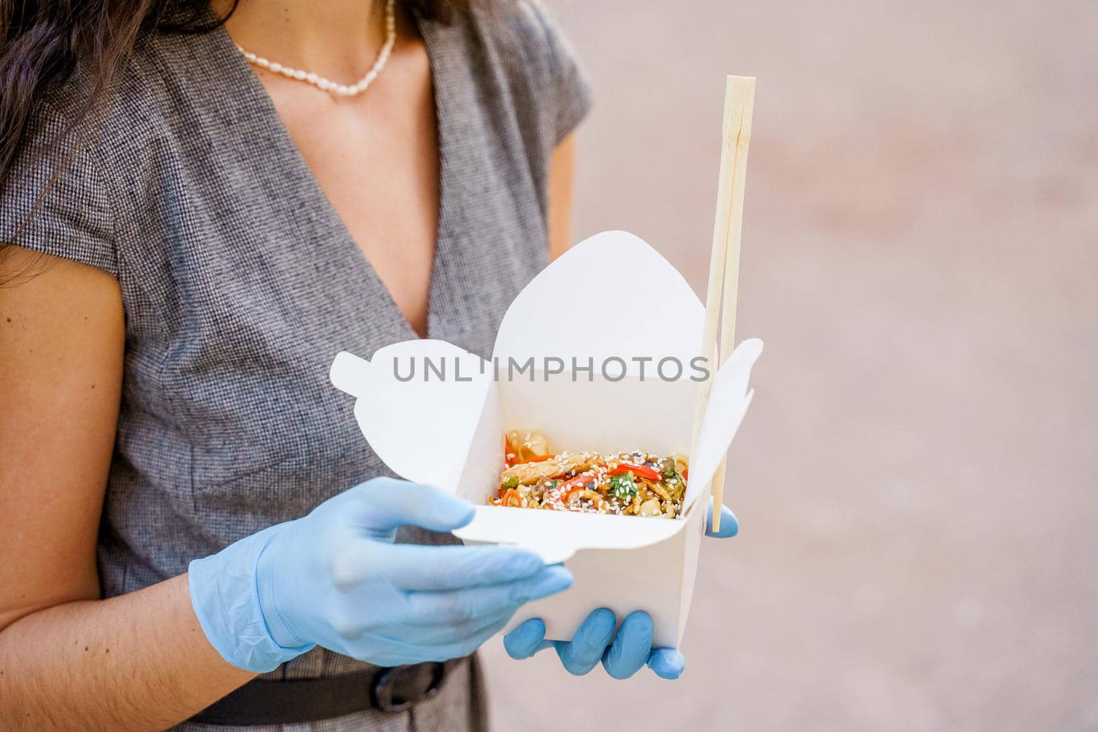 Closeup tasty food wok in box delivery. Girl holds udon noodles with in hands in medical gloves. Japanese spicy food in disposable eco boxes.