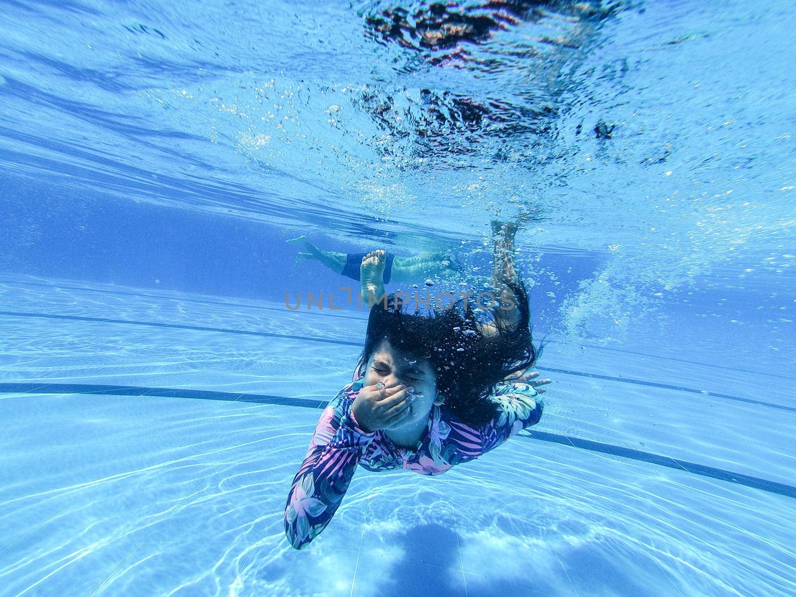 little girl creates bubbles under water in the pool. by Peruphotoart