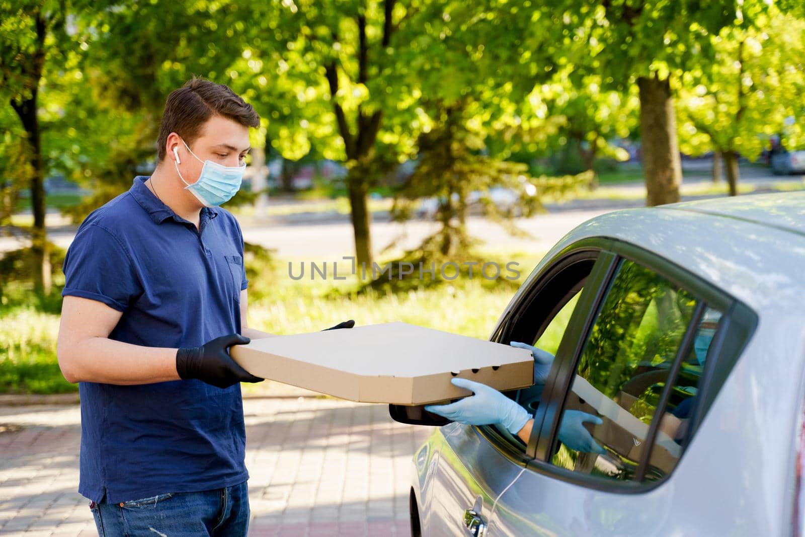 Food delivery courier gives pizza to woman in eco car. Tasty pizza with salami, cheese, tomatoes in cardoard box. Giving food trought car window