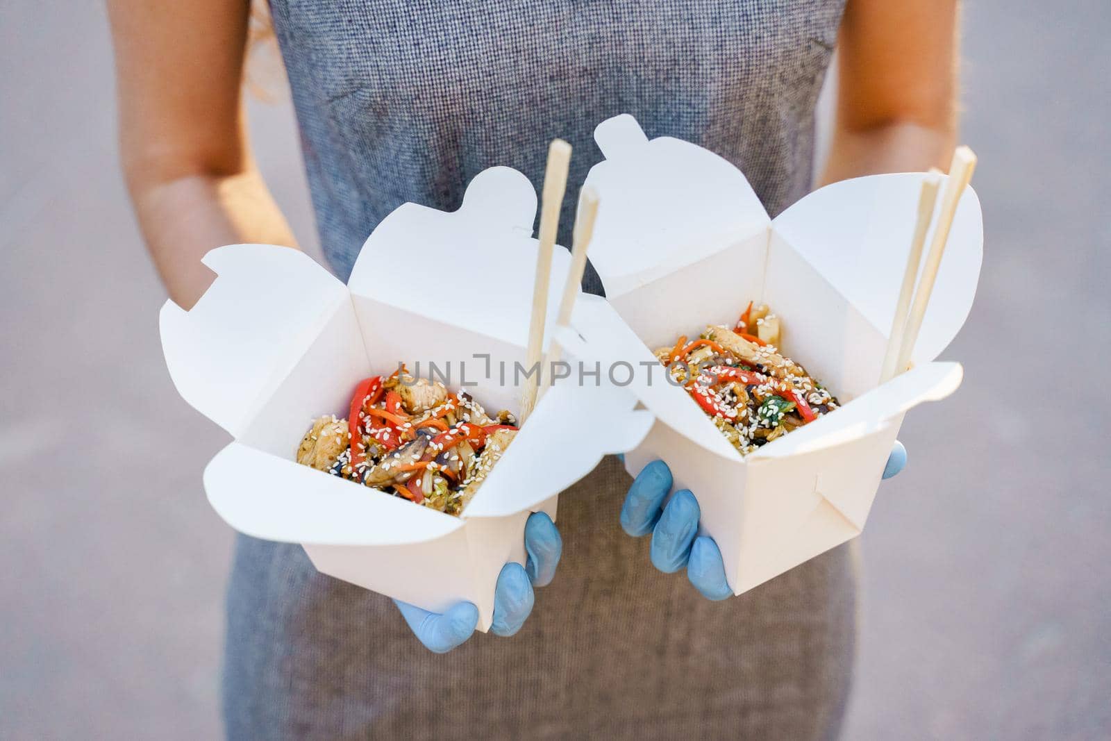 Closeup tasty food wok in box delivery. Girl holds udon noodles with tempuru, shrimps, soy sauce in hands. Chinese spicy food in disposable eco boxes by Rabizo