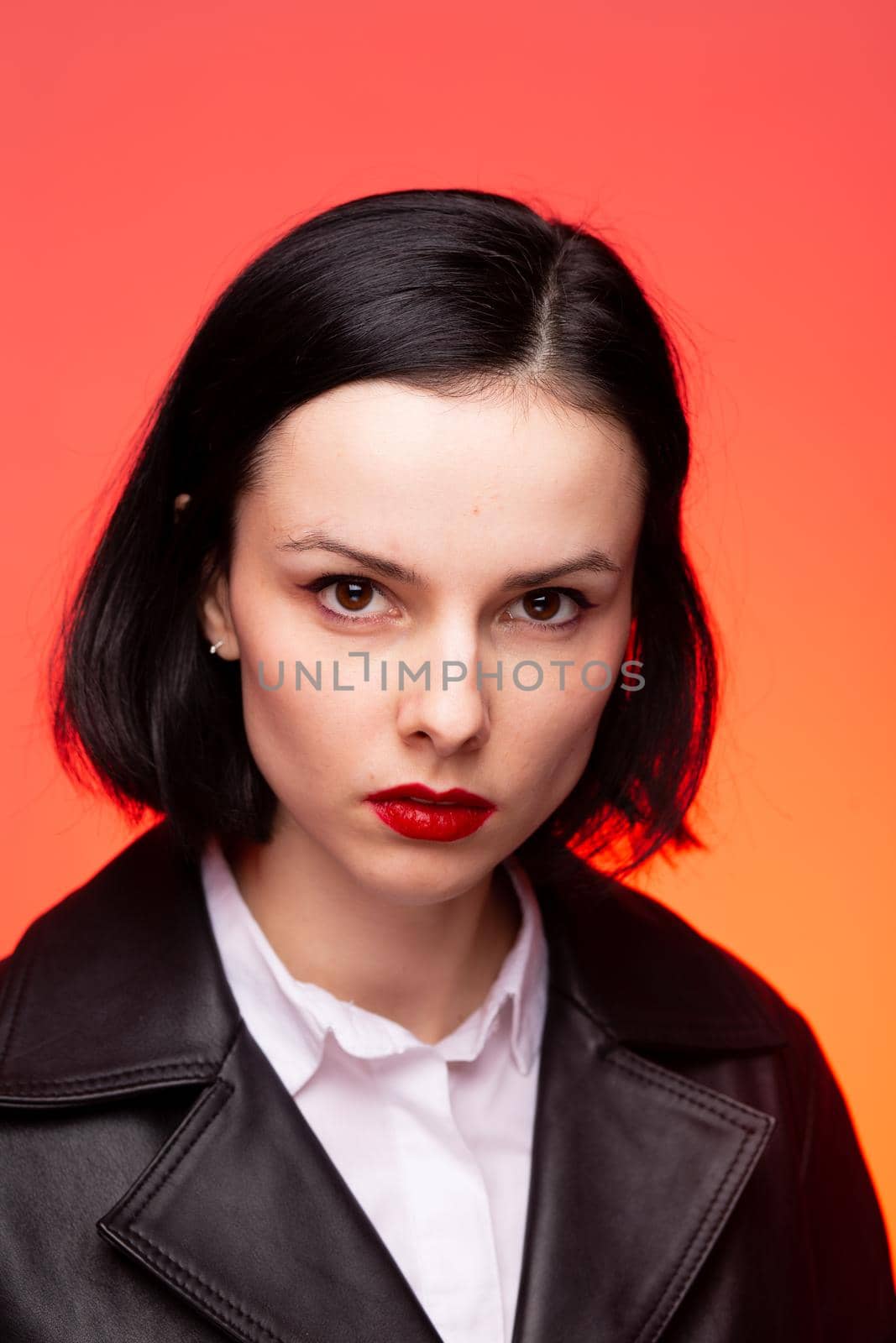 brunette woman with red lipstick on her lips in a black leather jacket and white shirt, red background by shilovskaya
