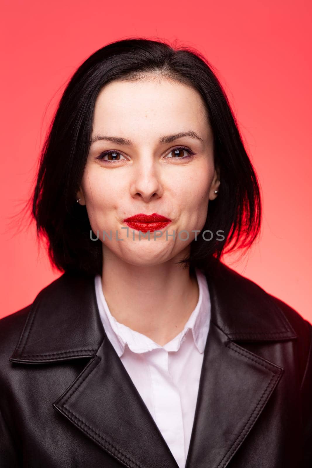 brunette woman with red lipstick on her lips in a black leather jacket and white shirt, red background by shilovskaya