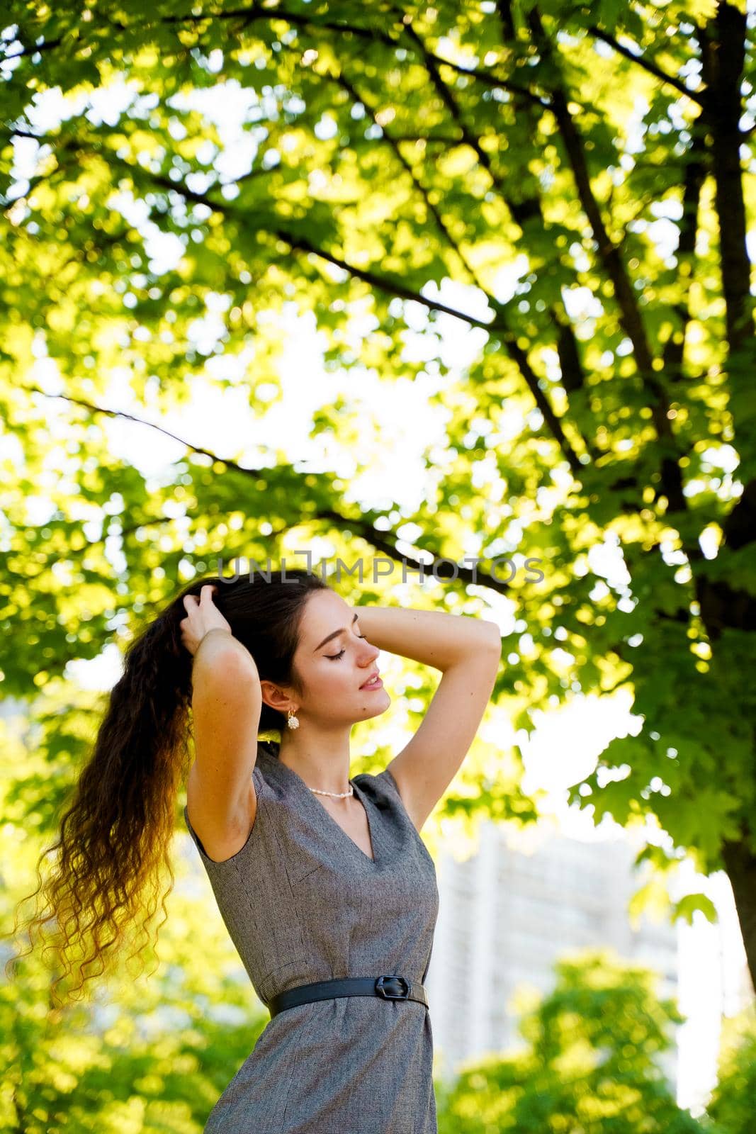 Relaxation and meditation lifestyle of young girl in green park. Vertical photo of beautiful girl who touches and correct her hair.