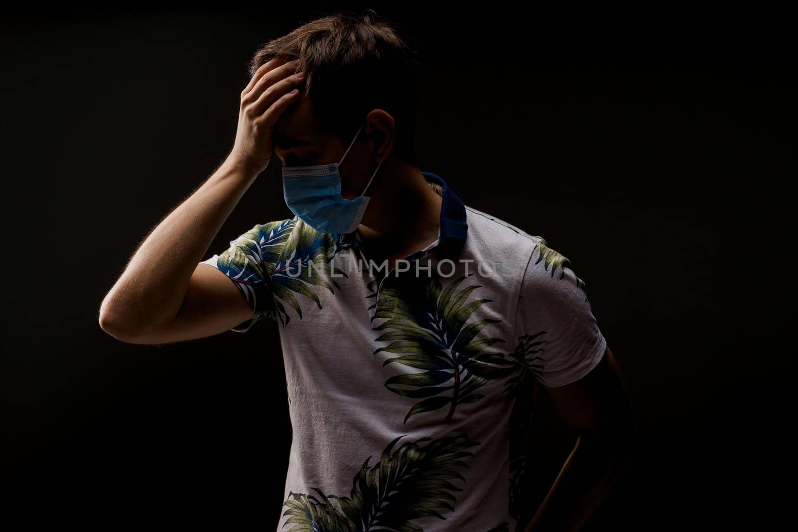 Headache man in blue medical mask isolated black background. Man touches her head because sicks coronavirus covid-19. Pandemic 2020 by Rabizo