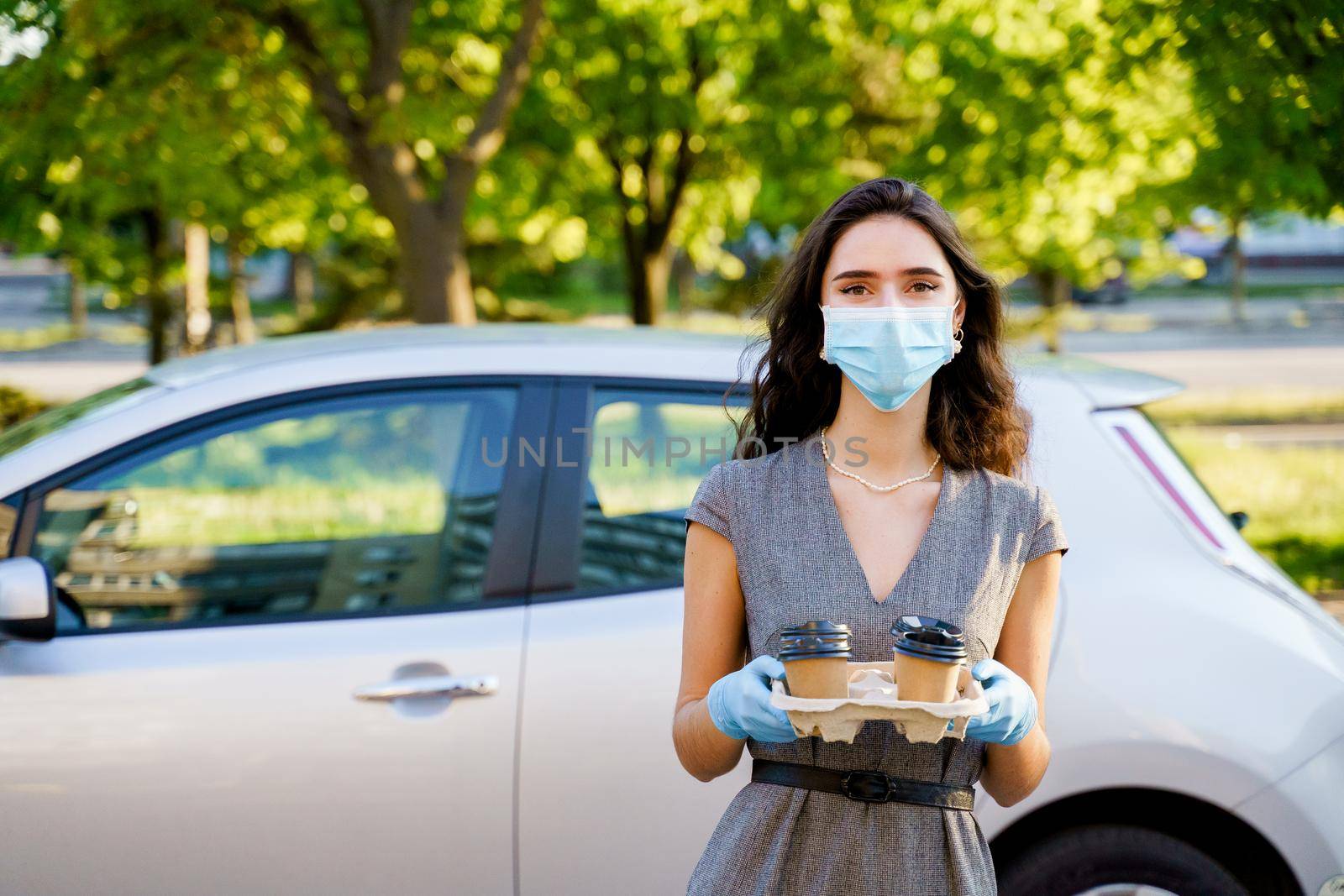 Coffee from coffee shop delivery by car. Coffee in eco disposable cardboard cup. Young girl works in delivery agency. 4 coffee in hands.