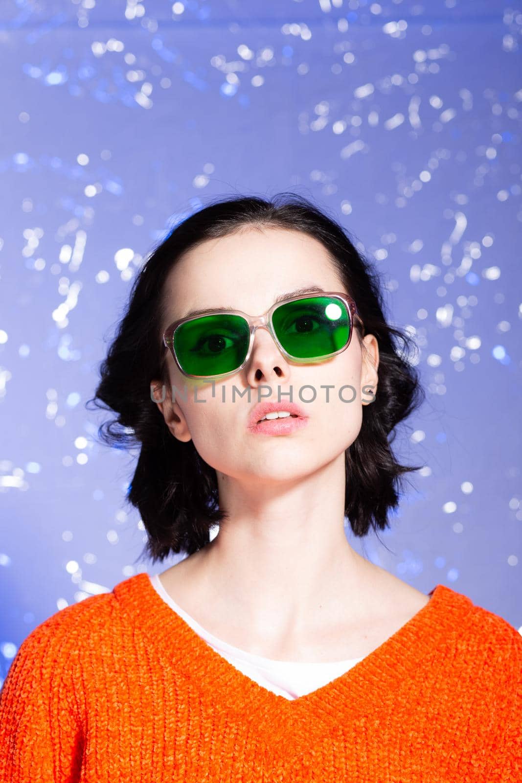 beautiful girl in an orange sweater and green glasses on a blue background. High quality photo