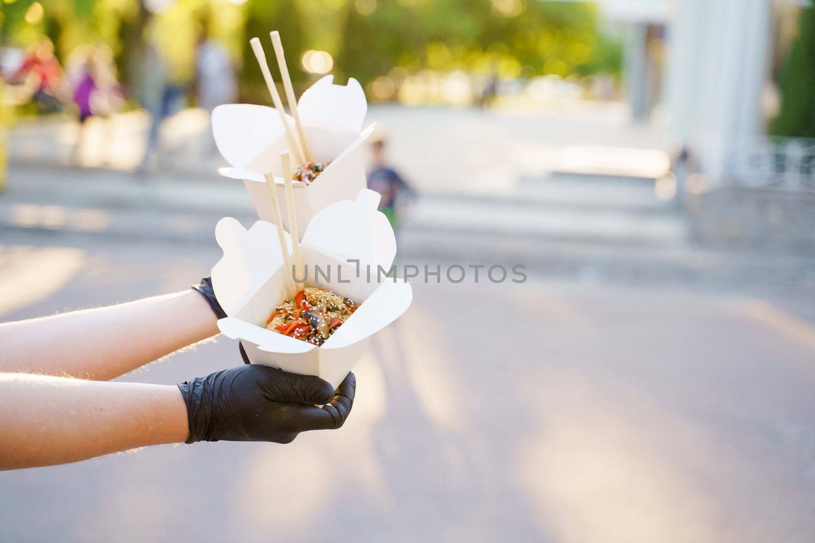 Closeup tasty food wok in box delivery. Man holds udon noodles with chopsticks in black medical gloves. Chinese spicy food in disposable eco boxes.