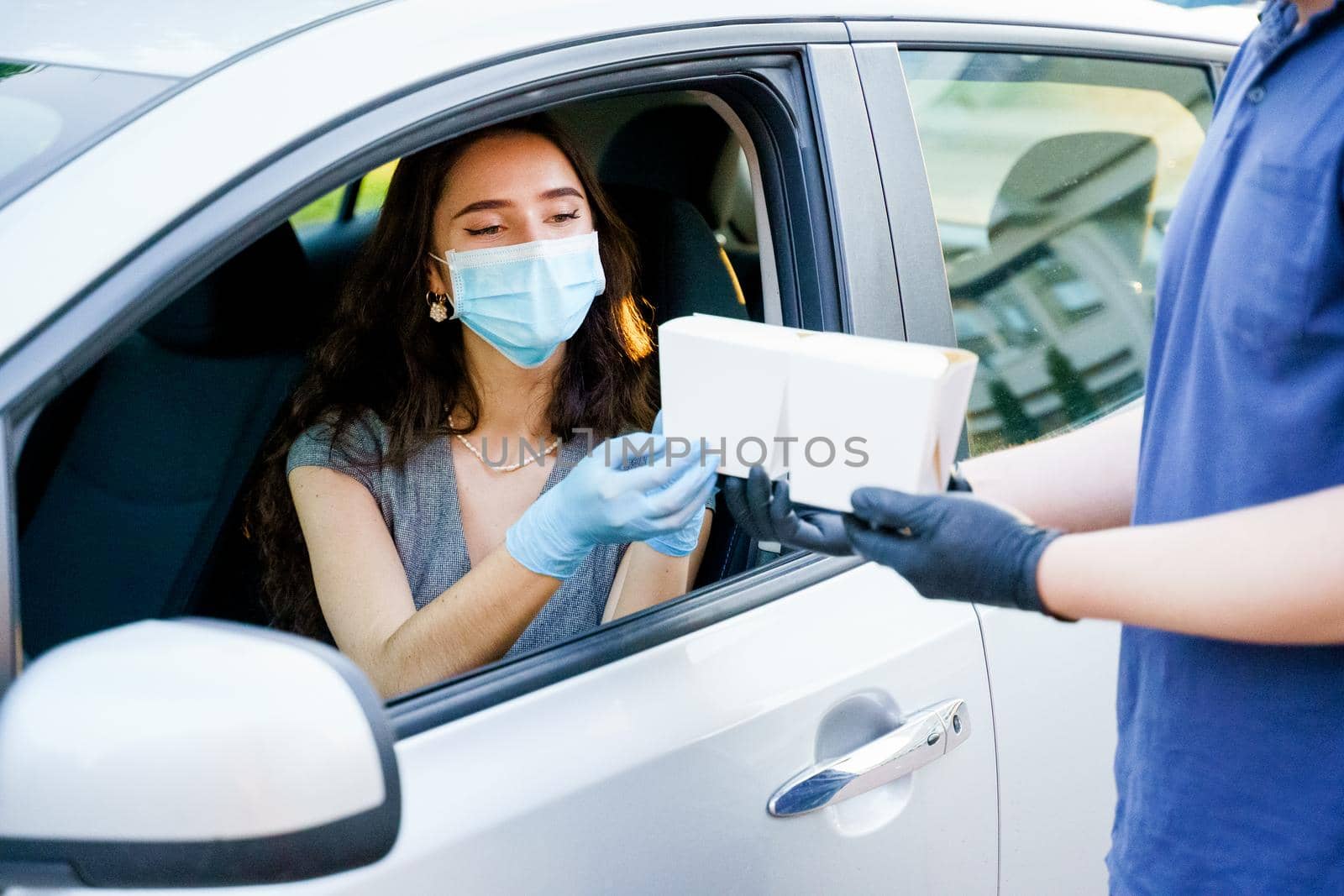 Udon noodles in white box delivery. Young attractive girl in car in medical gloves and mask holds wok in box udon noodles and smiles