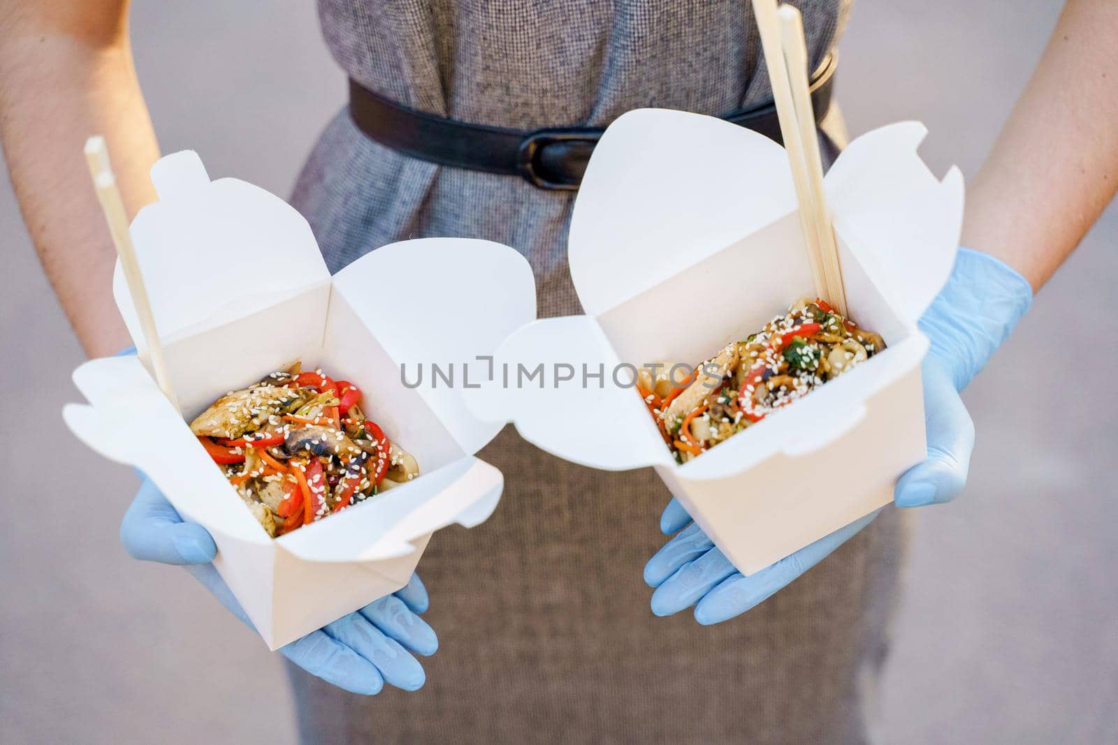 Closeup tasty food wok in box delivery. Girl holds udon noodles with tempuru, shrimps, soy sauce in hands. Chinese spicy food in disposable eco boxes.