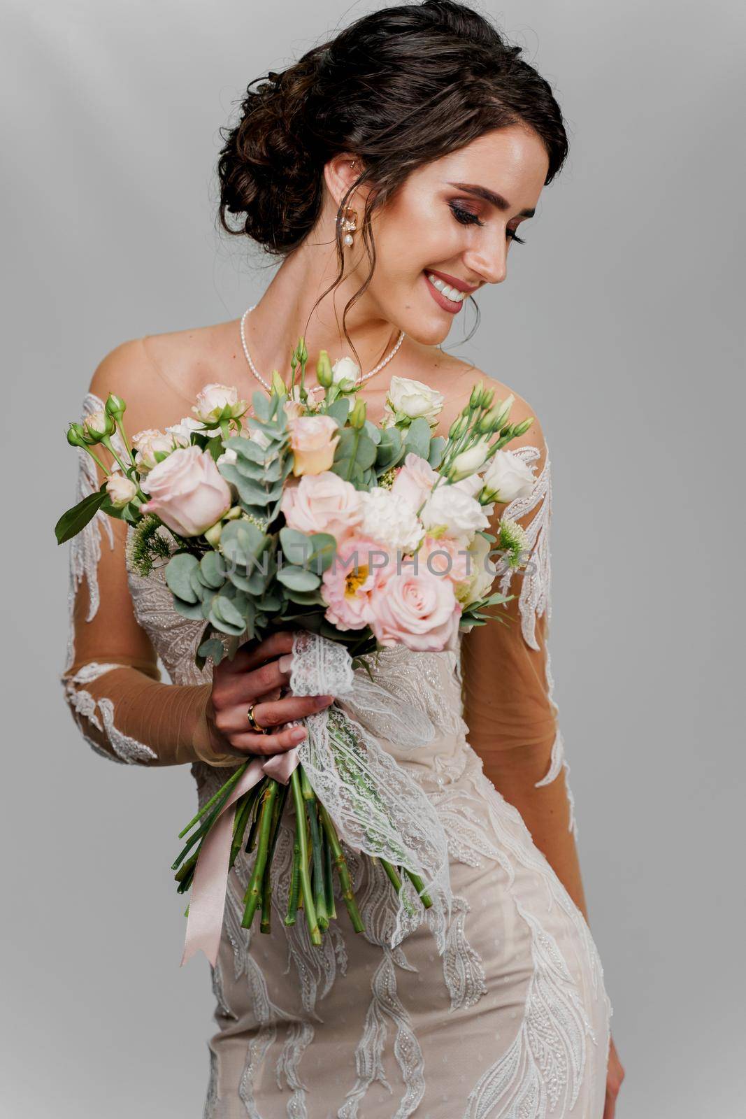 Bride with wedding bouquet looks right side and smiles. Attractive girl vertical portrait for social networks. Girl in wedding gown on blank background.