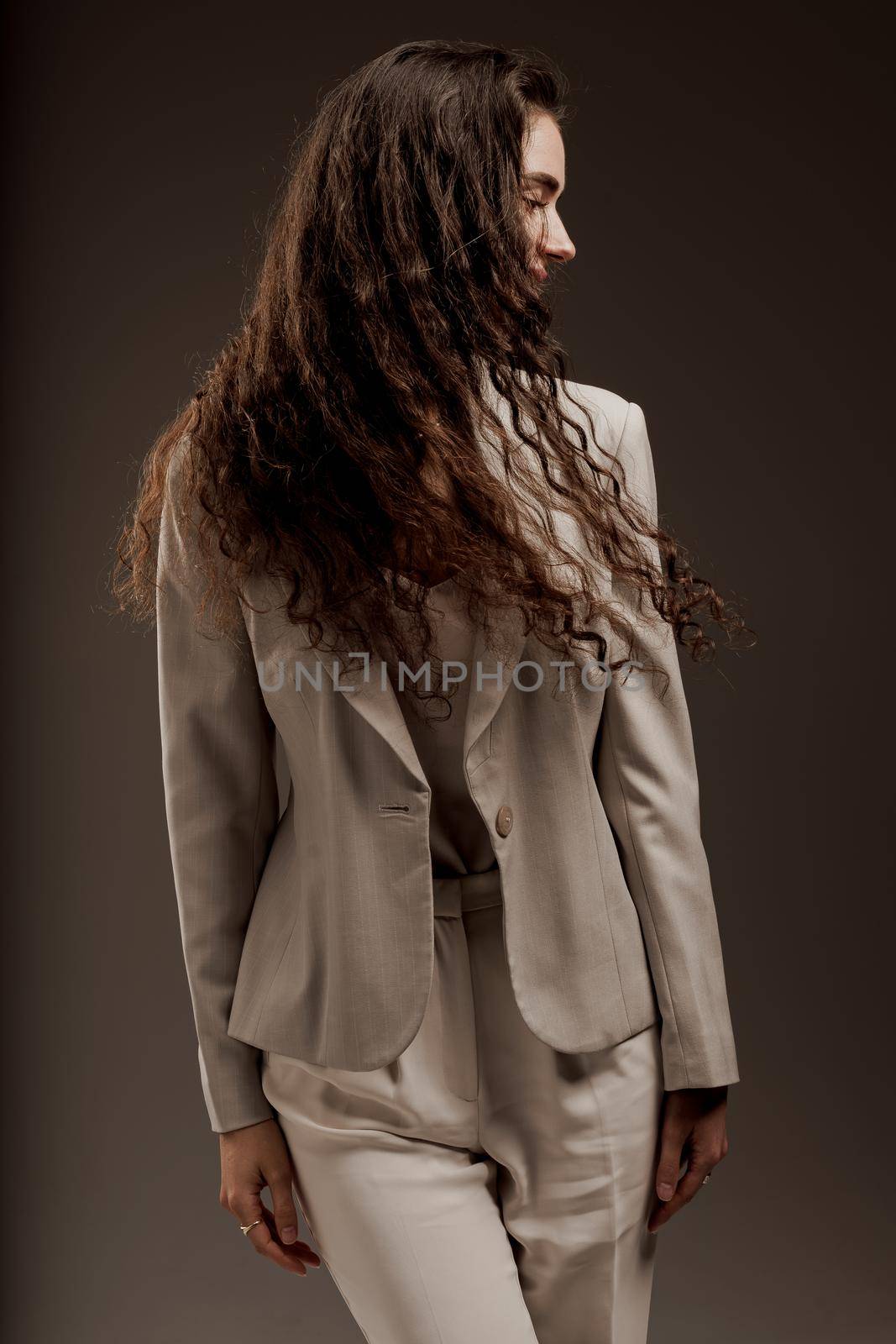 Gorgeous young female in classic suit in photostudio. Fashion, elegant and sexy professional model in studio. Attractive girl with curly hair posing