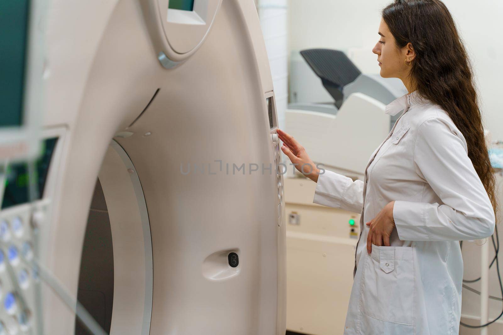 Medical doctor does computer tomography fot patient. Young girl in white coat looks in CT and press button to start procedure research diagnostic